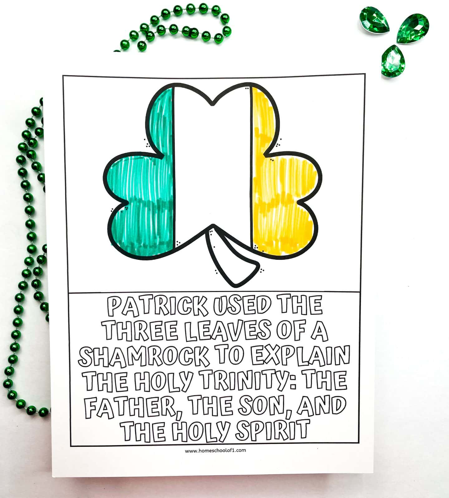 A St. Patrick’s Day coloring worksheet featuring a large shamrock with one leaf colored green, one yellow, and one uncolored. The caption below reads, “Patrick used the three leaves of a shamrock to explain the Holy Trinity: the Father, the Son, and the Holy Spirit.” Green bead garland and three green gem decorations are arranged around the page.

