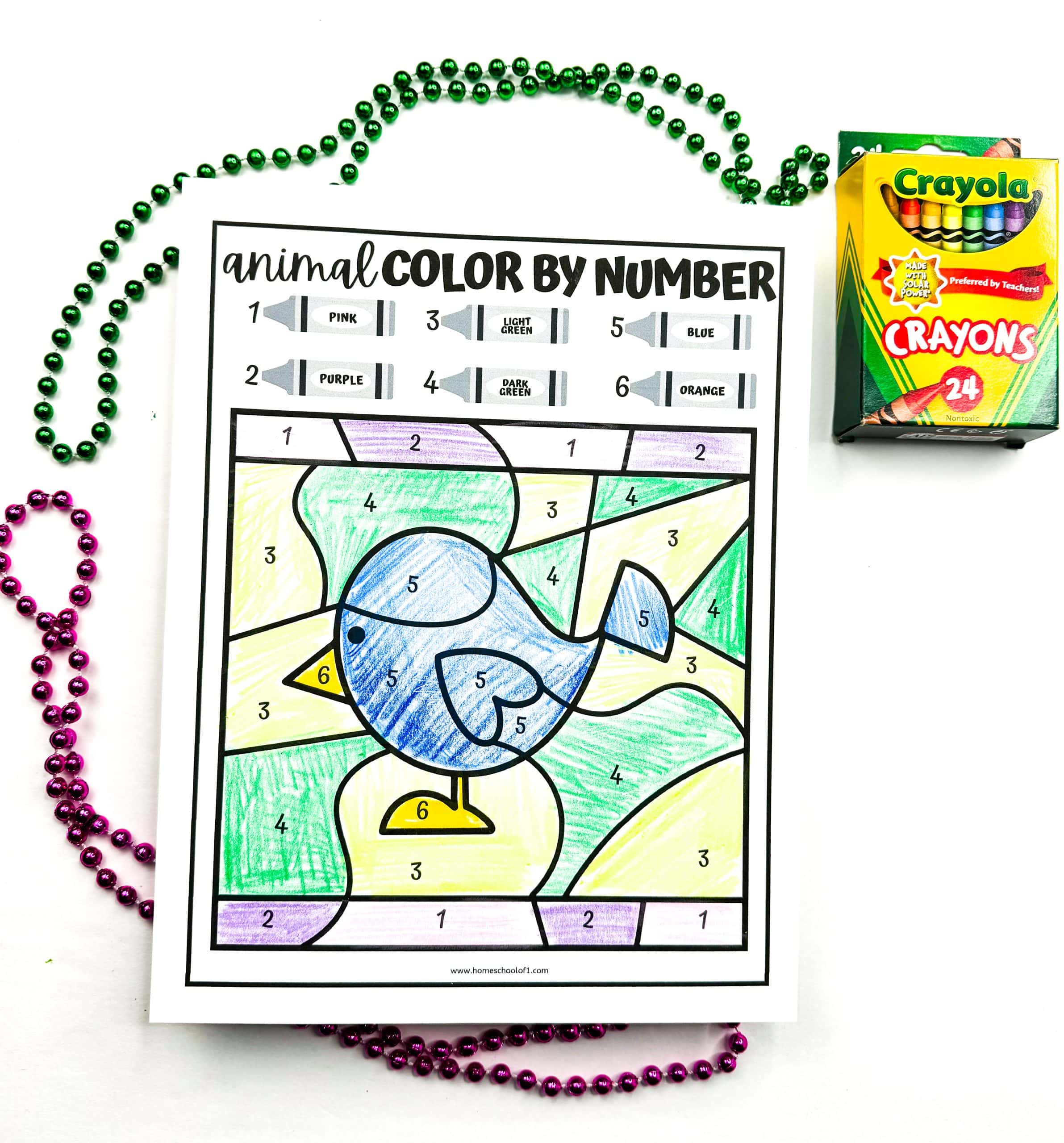 A completed animal color by number worksheet showing a cartoon bird colored with crayons in blue, yellow, light green, dark green, purple, pink, and orange, matching the number key at the top. The worksheet is surrounded by green and purple bead necklaces, with a 24-pack of Crayola crayons in the upper right corner.