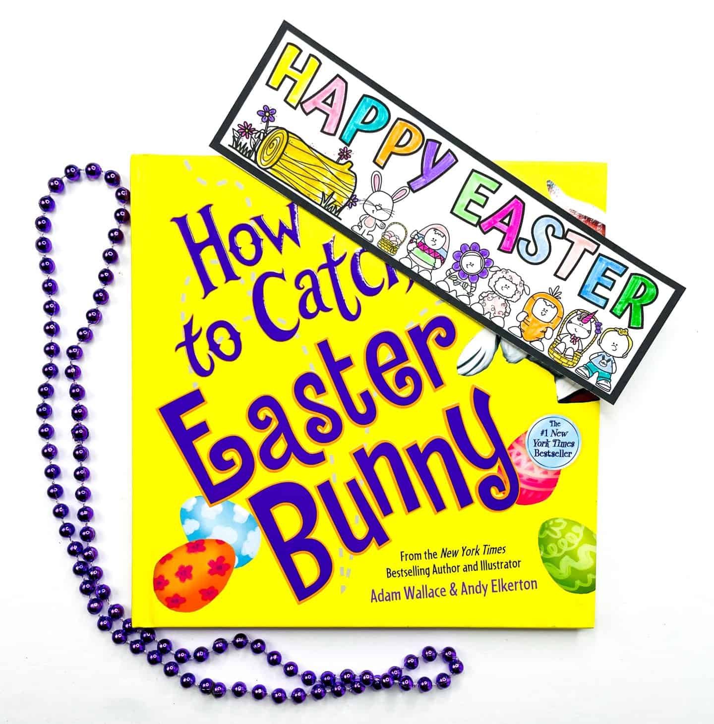 A bright yellow Easter book titled How to Catch the Easter Bunny is topped with a colorful “Happy Easter” bookmark featuring cartoon characters and Easter symbols. A strand of shiny purple beads adds a festive touch.

