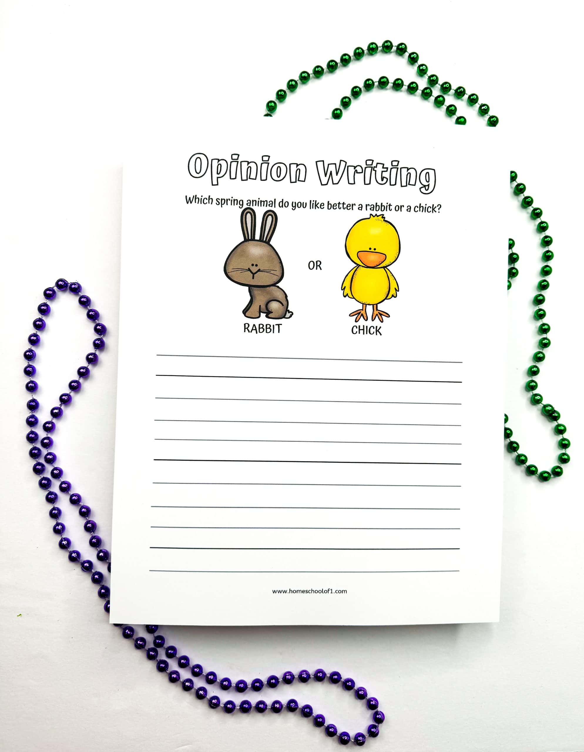 An “Opinion Writing” worksheet for kids asks the question, “Which spring animal do you like better: a rabbit or a chick?” It features cute colored illustrations of a brown rabbit and a yellow chick with labeled options, and lined space below for writing. The page is placed on a white surface decorated with green and purple beaded necklaces, adding a festive spring vibe.


