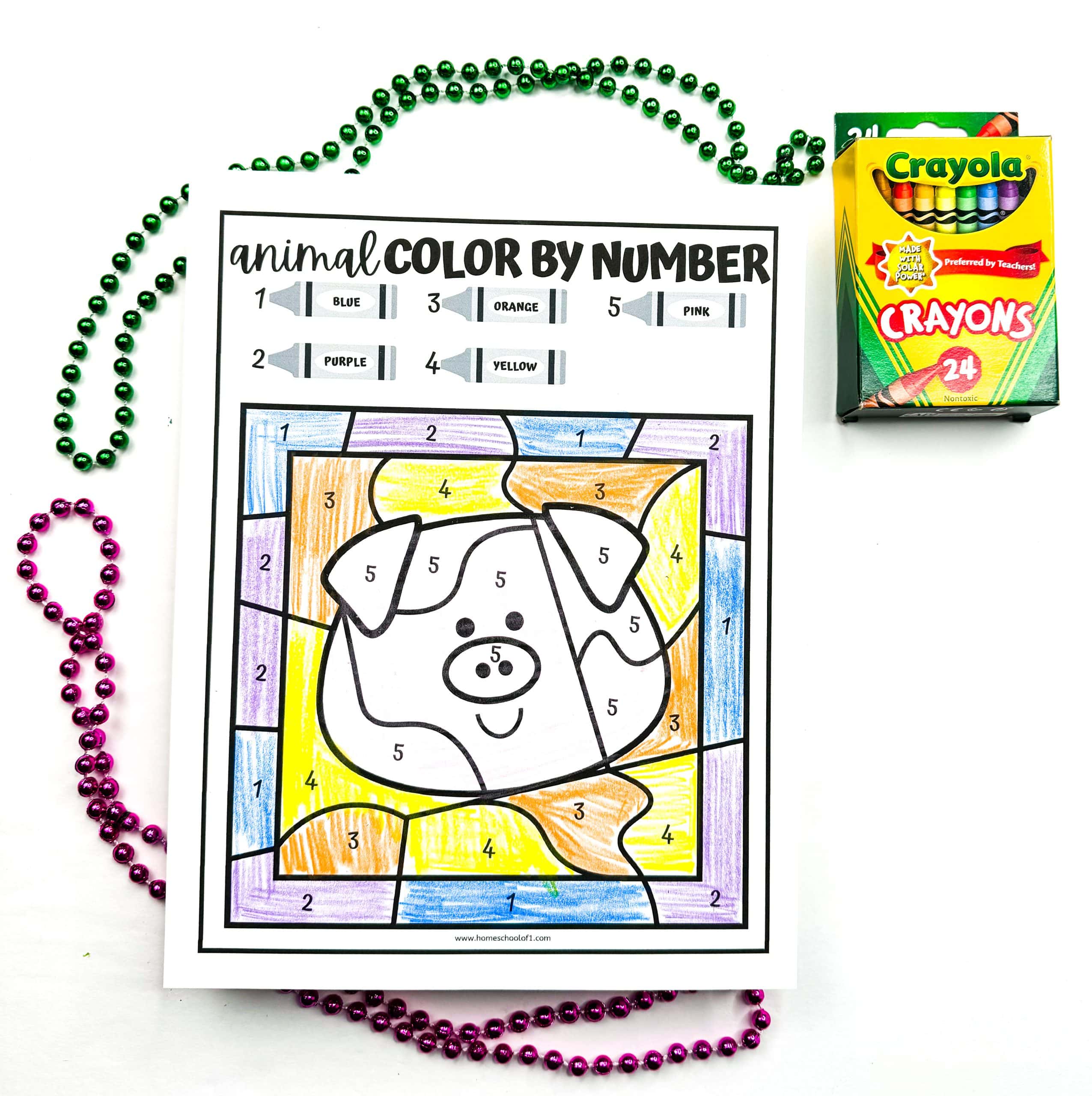 A completed animal color by number worksheet featuring a cartoon pig colored with blue, purple, orange, yellow, and pink crayons according to the number guide. The worksheet is surrounded by green and purple beaded necklaces, and a 24-count box of Crayola crayons is placed to the right.