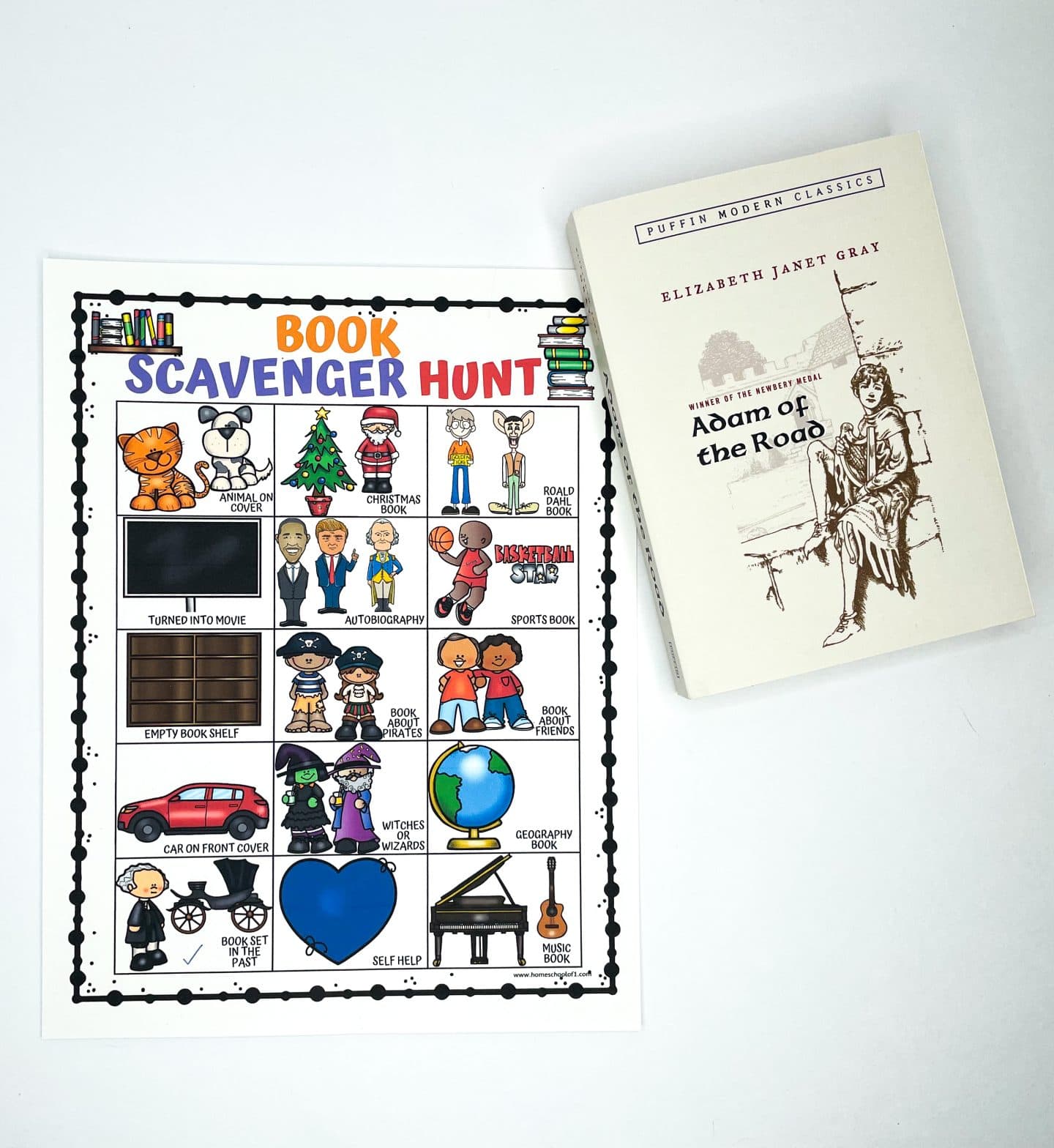A printable Book Scavenger Hunt sheet lies flat on a white surface next to a copy of Adam of the Road by Elizabeth Janet Gray. The scavenger hunt features illustrated prompts like “Animal on Cover,” “Turned into Movie,” “Book Set in the Past,” and “Book About Pirates.” The activity encourages kids to explore various genres and themes during library visits or reading time. The book beside it fits the historical category in the scavenger hunt.