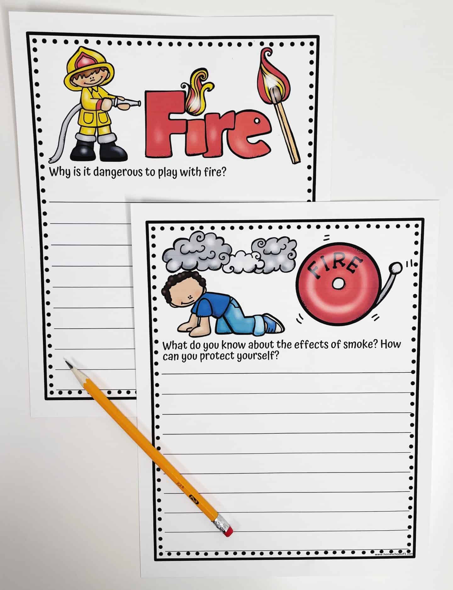 The image features two fire safety worksheets with colorful illustrations. The first worksheet includes a firefighter and a matchstick with the word "Fire" in large, bold letters. The prompt asks, "Why is it dangerous to play with fire?" The second worksheet shows a child crawling under smoke with a fire alarm illustration, accompanied by the question, "What do you know about the effects of smoke? How can you protect yourself?" A yellow pencil is placed beside the worksheets, and both pages have dotted borders and lines for students to write their responses.