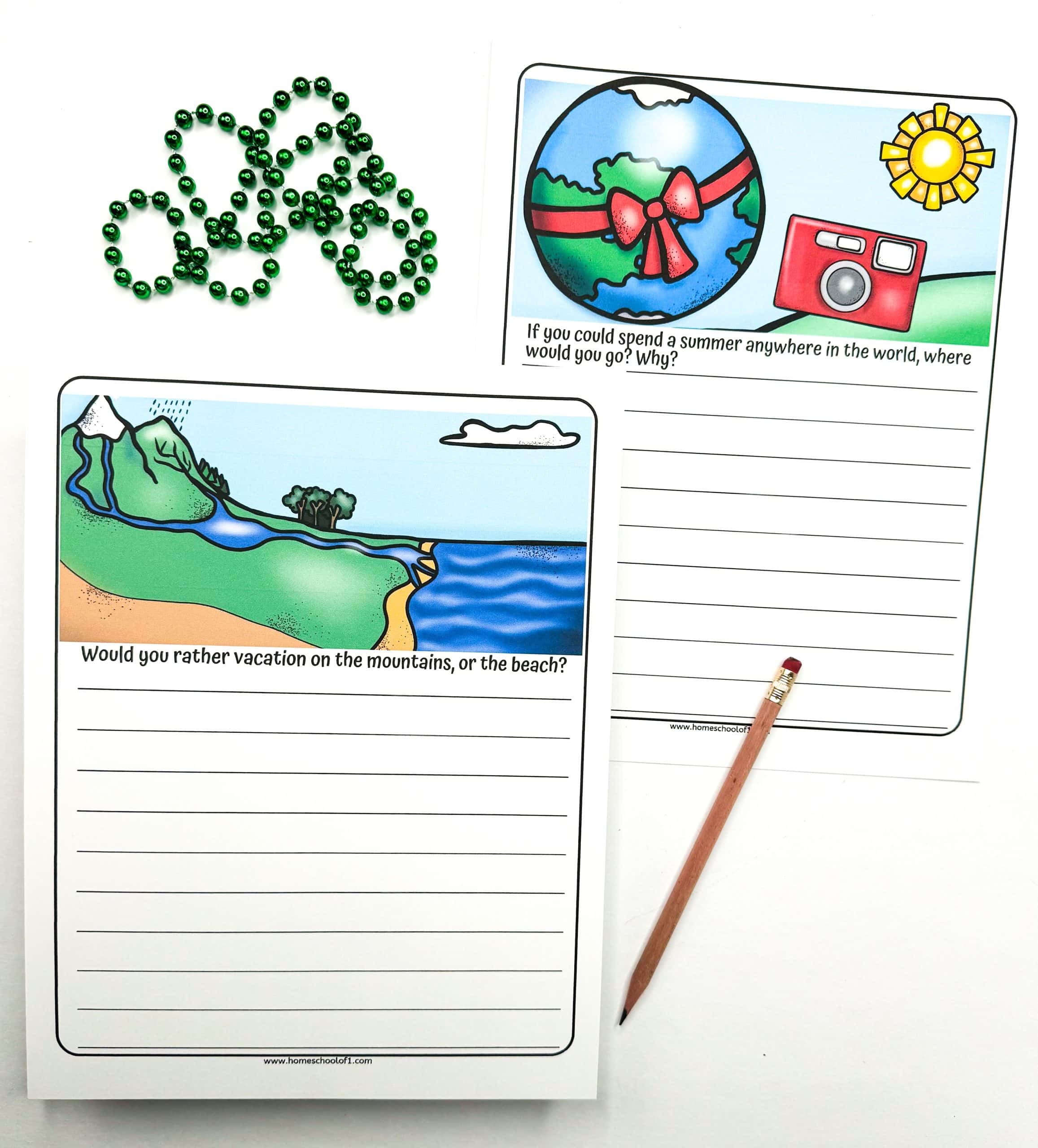 Two free printable summer writing prompts for kids with colorful travel-themed illustrations. One prompt asks, “Would you rather vacation on the mountains, or the beach?” and the other says, “If you could spend a summer anywhere in the world, where would you go? Why?” A green beaded necklace and a pencil are also visible.