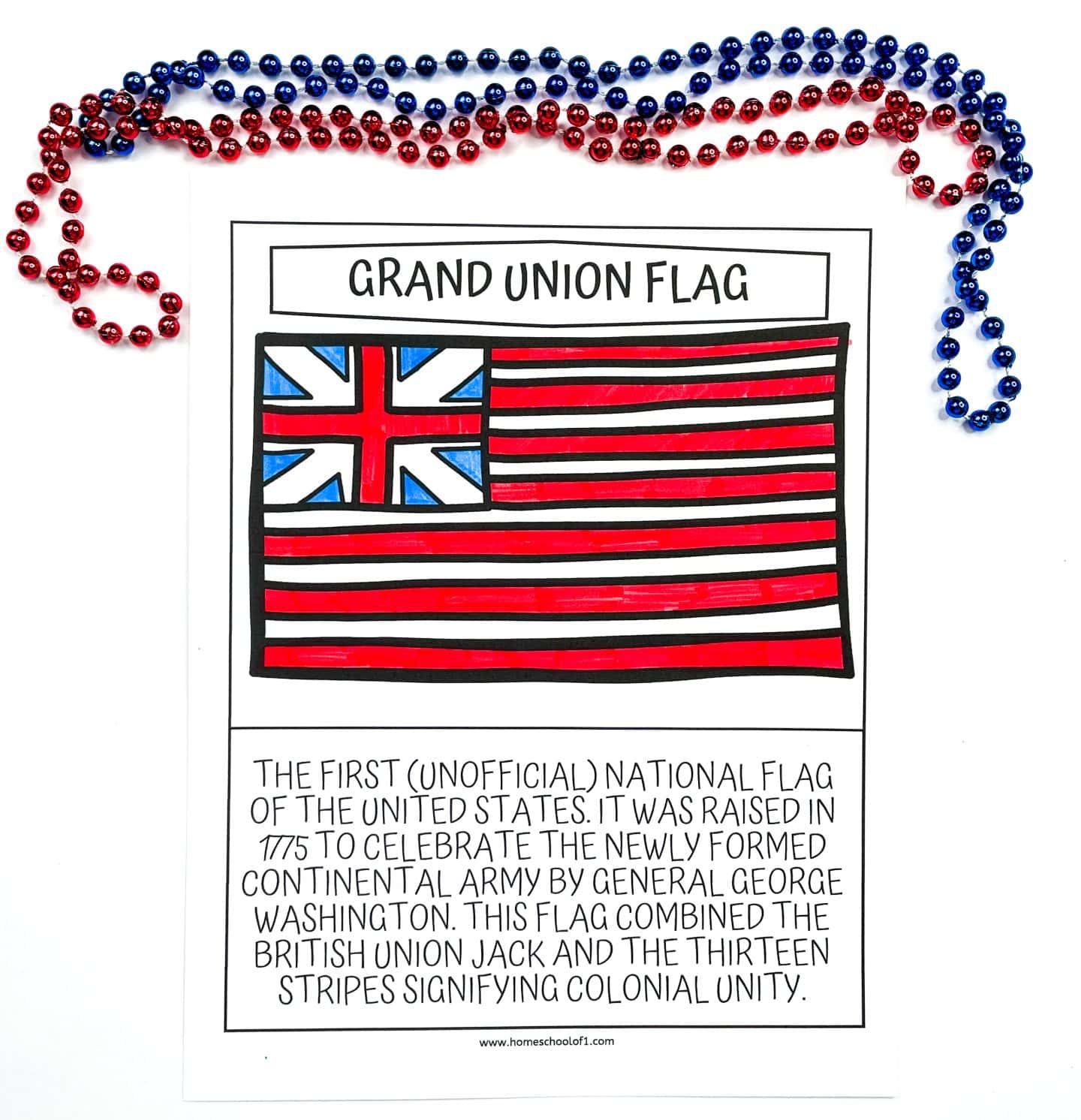 A coloring worksheet of the Grand Union Flag, which features thirteen red and white stripes and a British Union Jack in the corner, colored with red, blue, and black markers. The text below explains that this was the first unofficial national flag of the United States, raised in 1775 by General George Washington to represent the newly formed Continental Army. Red and blue beaded necklaces are arranged above the worksheet.