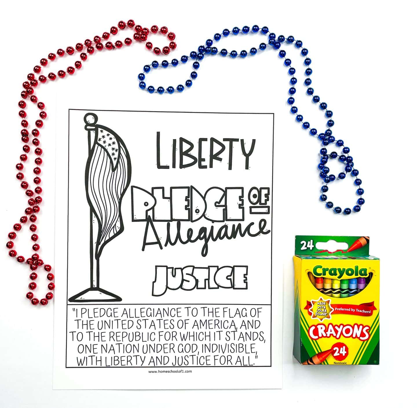 Black-and-white Pledge of Allegiance coloring sheet featuring a waving American flag and bold words like “Liberty,” “Justice,” and “Pledge of Allegiance.” The full pledge is written at the bottom for students to read or trace. Red and blue beaded necklaces and a box of Crayola crayons are arranged beside the worksheet on a white background.