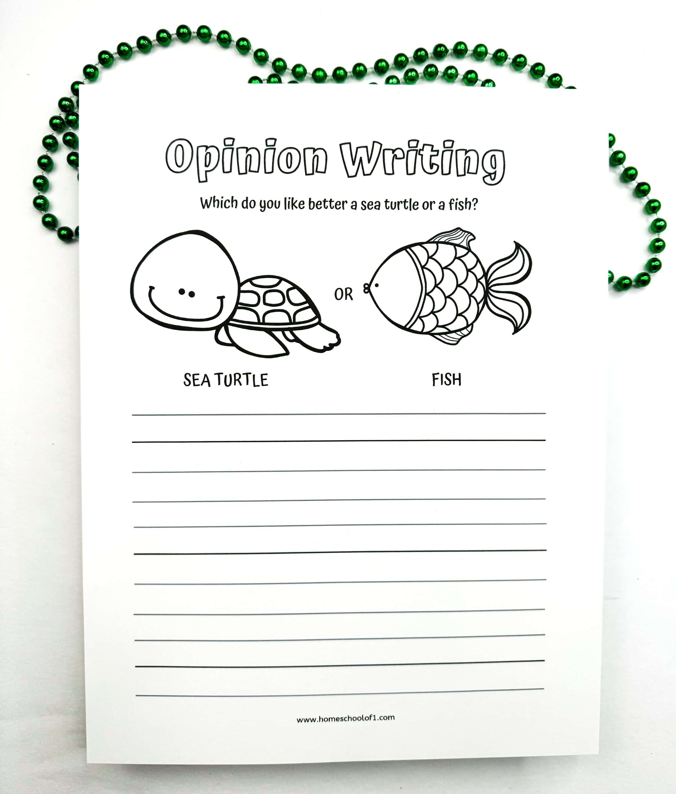 An “Opinion Writing” worksheet for kids that asks, “Which do you like better: a sea turtle or a fish?” with black-and-white illustrations of both animals above lined space for writing. The page is decorated with green beaded necklaces around the top and sides, adding a playful touch.