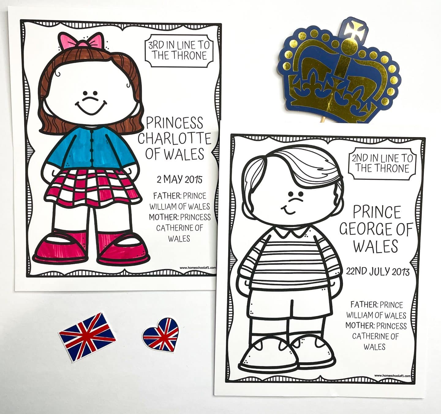 Two royal family coloring pages display cartoon-style drawings of Princess Charlotte of Wales and Prince George of Wales. Charlotte’s page is colored in with a pink plaid skirt, blue top, and pink shoes, labeled “3rd in Line to the Throne,” born May 2, 2015. George’s page is uncolored and labeled “2nd in Line to the Throne,” born July 22, 2013. Both pages note their parents as Prince William and Princess Catherine of Wales. A paper crown and two small Union Jack decorations, one shaped like a heart, are also visible.