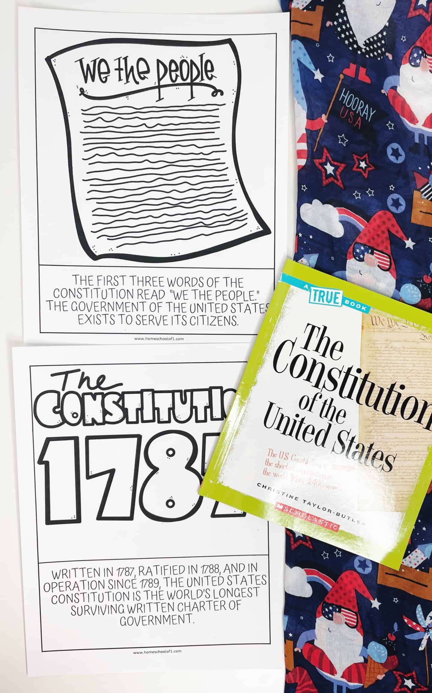 Two educational worksheets about the U.S. Constitution, one with the phrase "We the People" and the other with "The Constitution 1787," alongside a book titled "The Constitution of the United States" and festive gnome-patterned fabric.