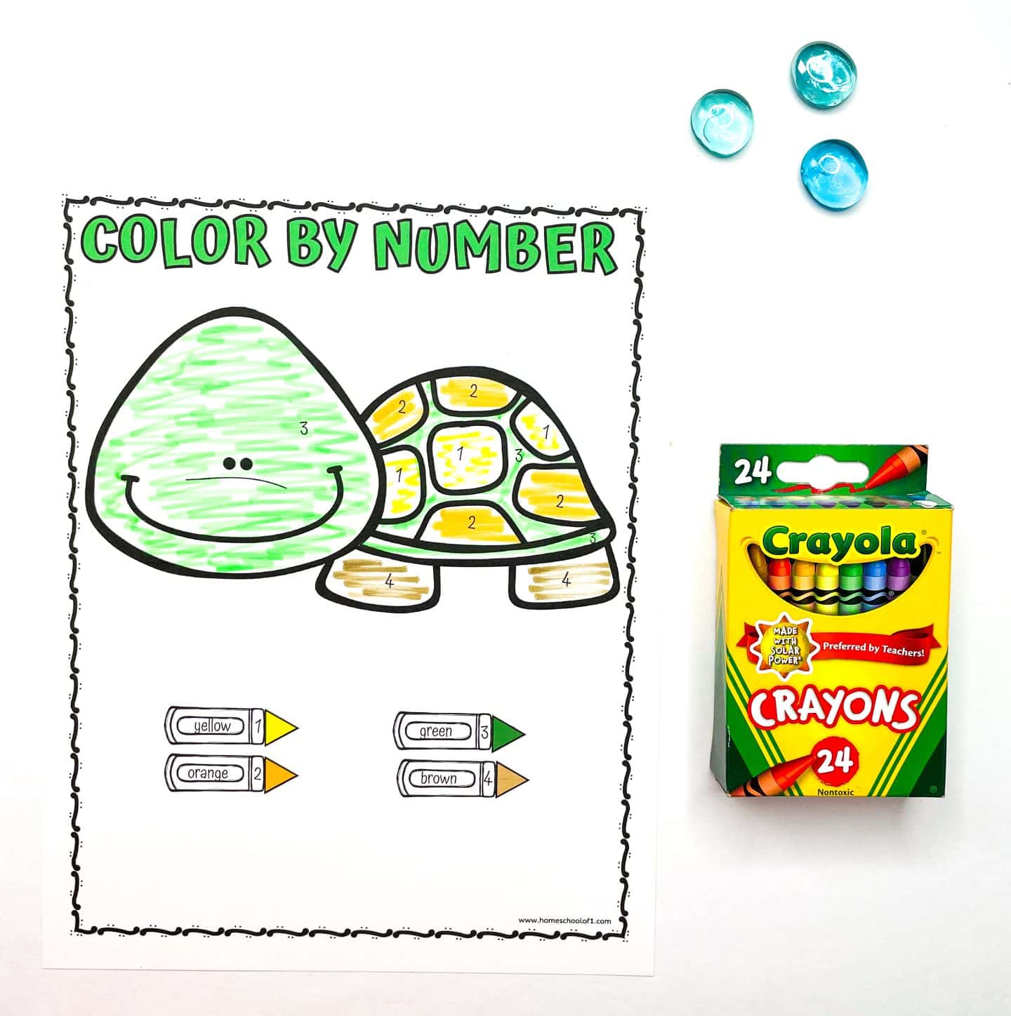 Preschool "Color by Number" worksheet featuring a smiling turtle with numbered sections colored in green, yellow, orange, and brown. The color key at the bottom shows which number corresponds to each color. To the right are a box of Crayola 24-count crayons and three blue glass counting gems.