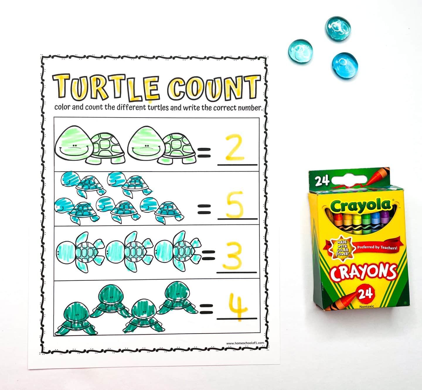 Turtle-themed preschool counting worksheet titled "Turtle Count," where children color and count groups of different turtle illustrations and write the correct number. Each row features a unique turtle design, with the answers written in yellow: 2, 5, 3, and 4. To the right of the worksheet are a box of Crayola crayons and three blue glass counting gems.