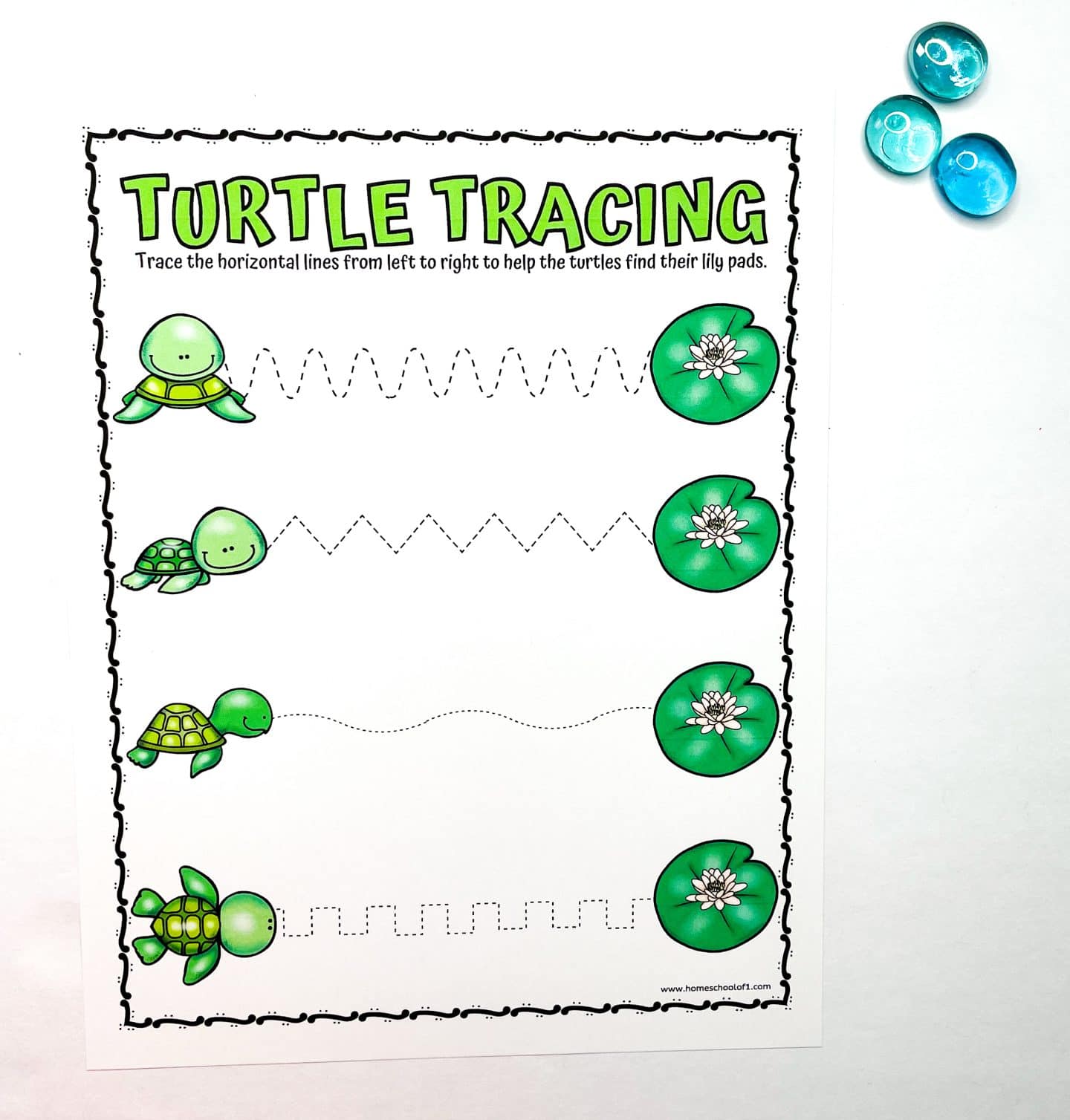Turtle-themed preschool tracing worksheet titled "Turtle Tracing" featuring four cute green turtles on the left and matching lily pads on the right. Children are instructed to trace different types of horizontal lines—zigzag, wavy, and boxy—to help the turtles reach their lily pads. Three blue glass counting gems are placed beside the worksheet.