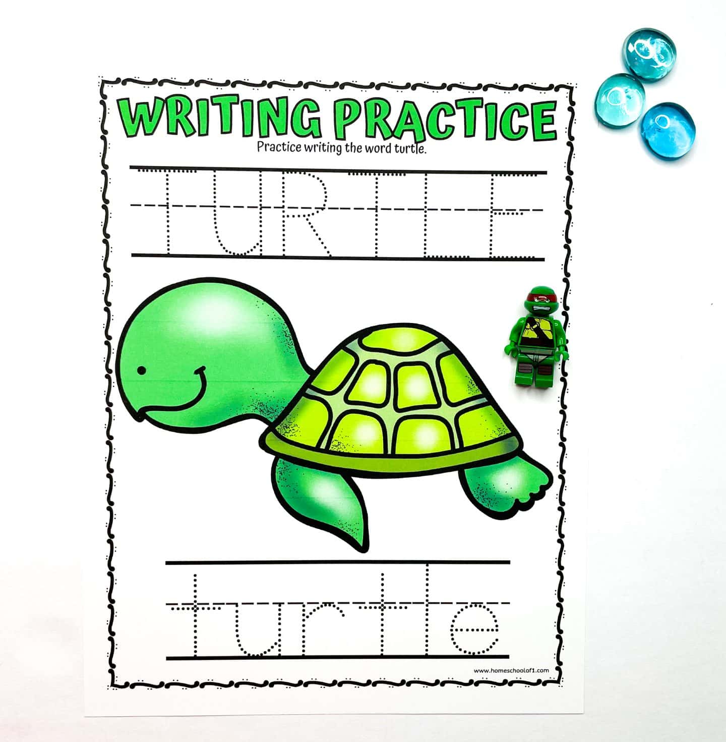 Turtle-themed preschool writing practice worksheet featuring the word “TURTLE” in both uppercase and lowercase dotted letters for tracing. A large, smiling green turtle illustration is centered on the page. To the right are a green turtle LEGO minifigure and three blue glass counting gems.