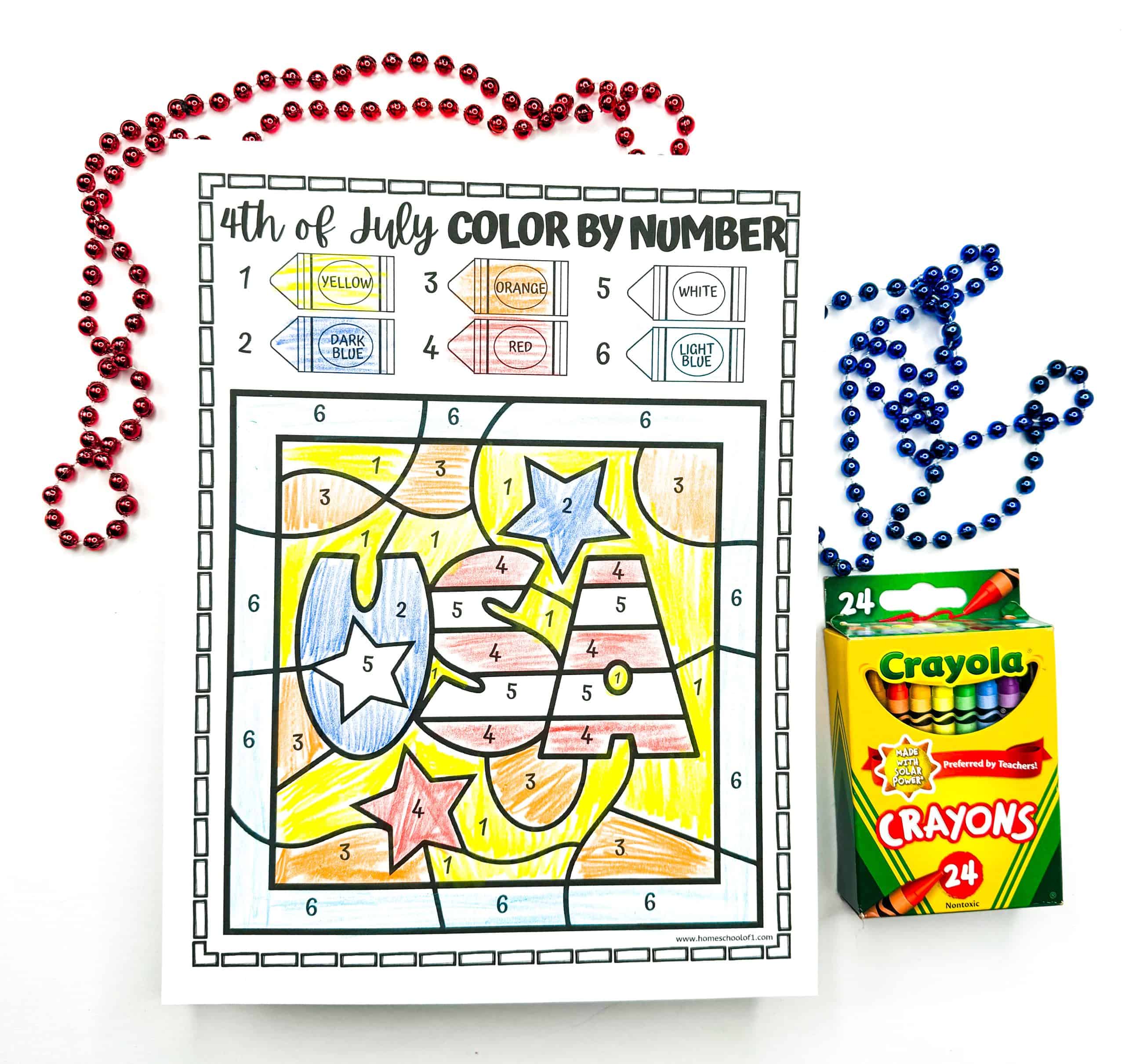 A completed 4th of July color-by-number worksheet features the word “USA” surrounded by stars, colored in red, white, blue, yellow, orange, and light blue based on a numbered crayon key. The page is bordered by festive red and blue bead necklaces, with a box of Crayola 24-count crayons placed to the right, enhancing the patriotic theme.
