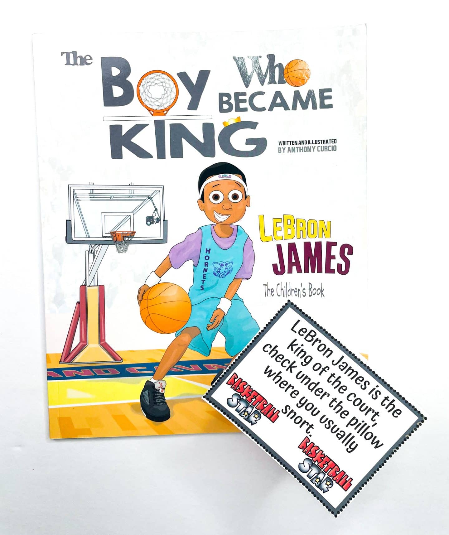 A children's book titled The Boy Who Became King: LeBron James is shown with a cartoon illustration of a young LeBron dribbling a basketball on a court. In front of the book is a basketball-themed scavenger hunt clue card that reads: “LeBron James is the king of the court, check under the pillow where you usually snort.” The card features small basketball player illustrations and the label “Basketball Star.”