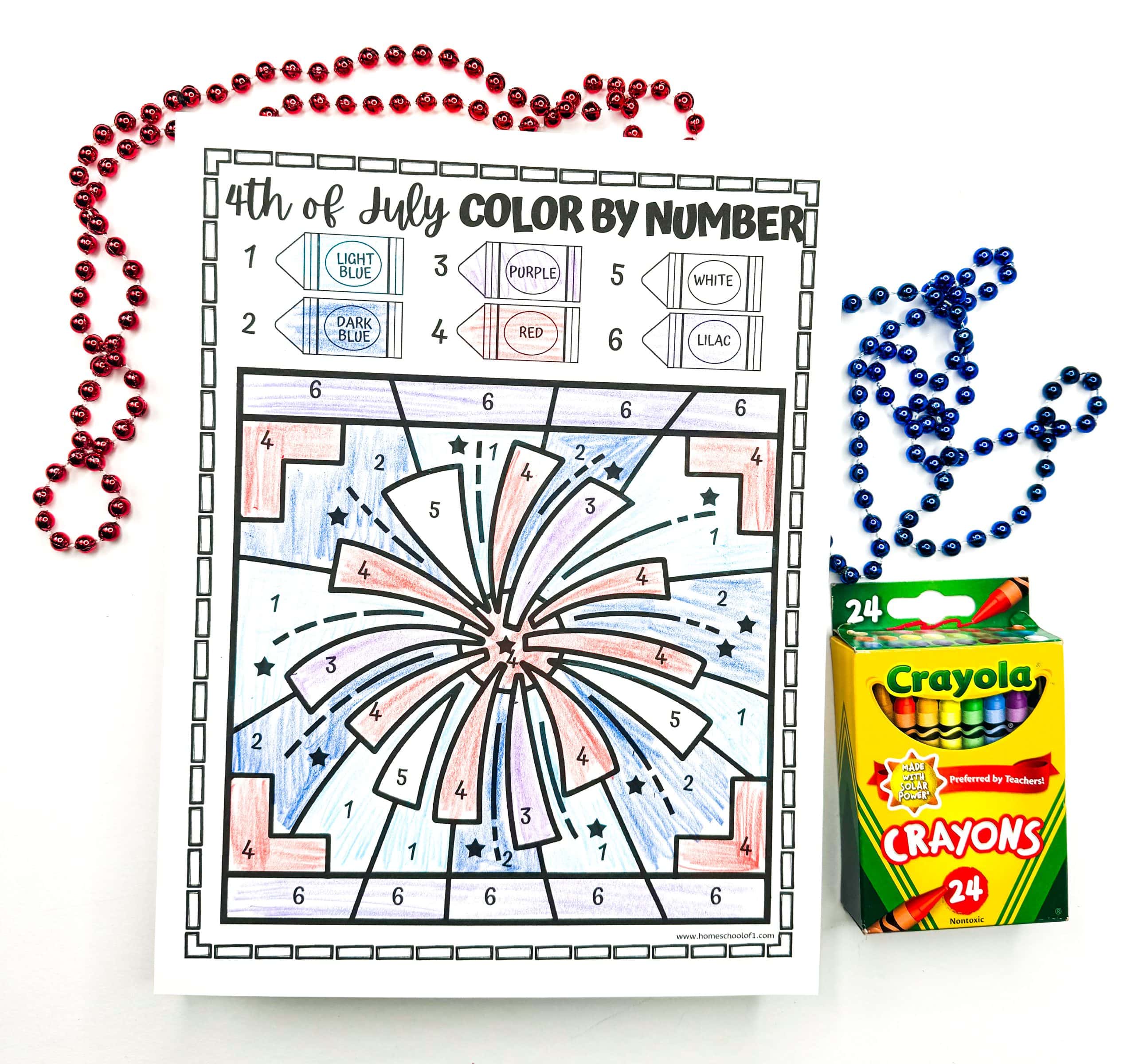 A finished 4th of July color-by-number worksheet features a large firework burst colored in shades of red, light blue, dark blue, purple, lilac, and white, based on the crayon key shown at the top. The festive scene is surrounded by red and blue bead necklaces and a box of Crayola crayons, adding to the patriotic and creative theme.