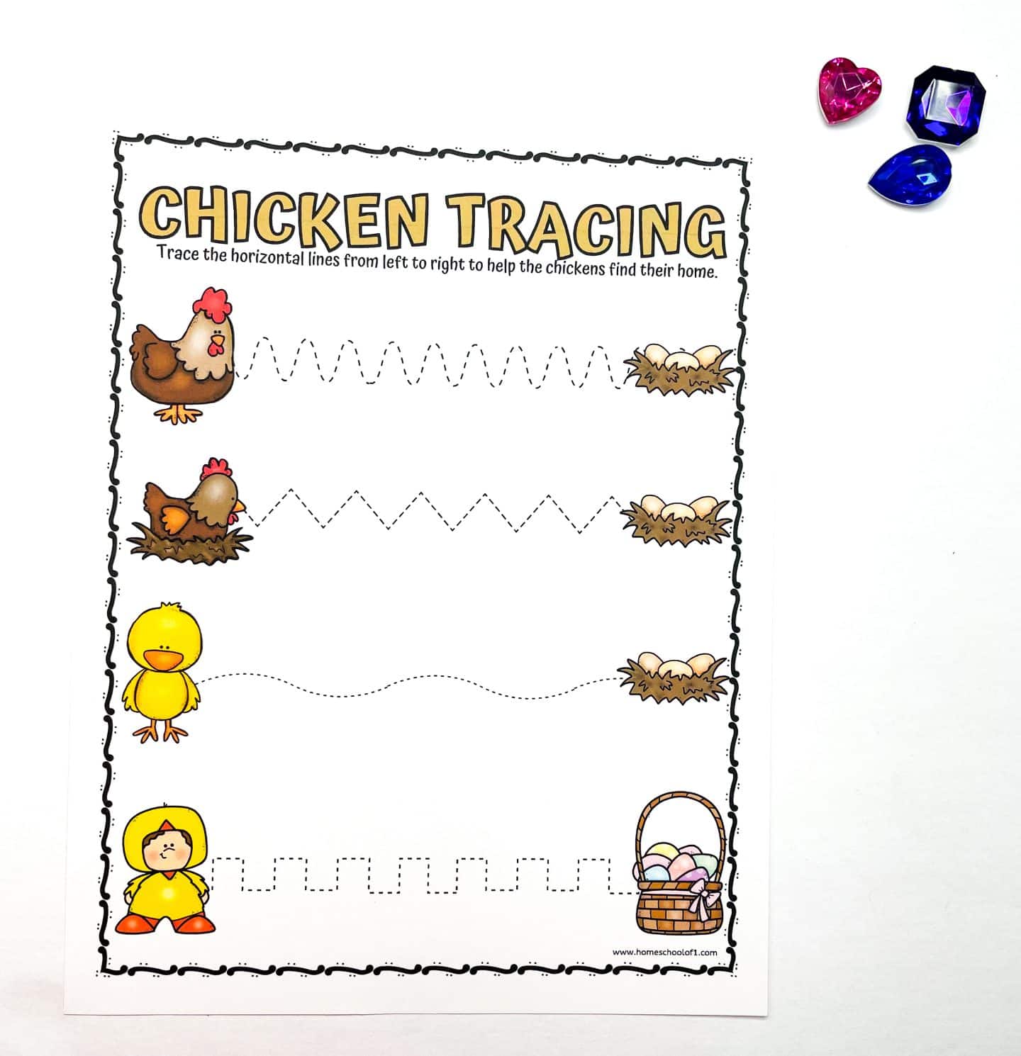 A chicken tracing activity sheet with three wavy paths leading from chickens to nests. Designed for children to practice tracing. Three decorative gems—pink, blue, and black—are placed above the sheet.

