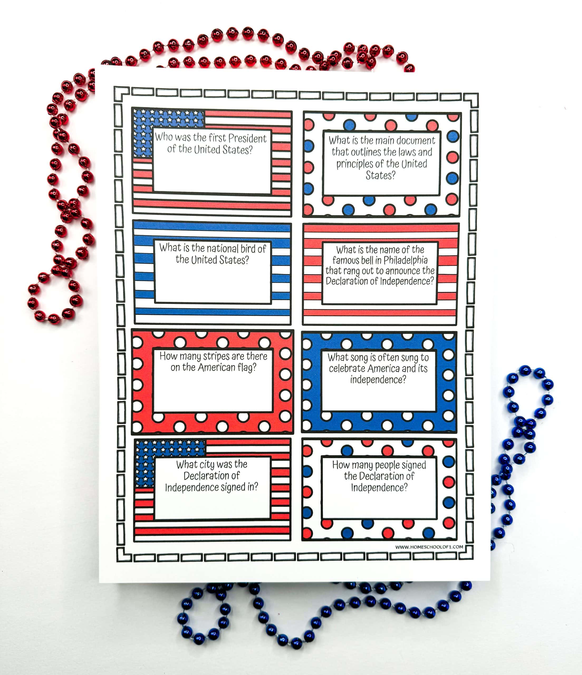 Patriotic red, white, and blue trivia card printables feature eight U.S. history questions, including “Who was the first President of the United States?” and “What city was the Declaration of Independence signed in?” The sheet is decorated with stars, stripes, and polka dots, and surrounded by red and blue bead necklaces.