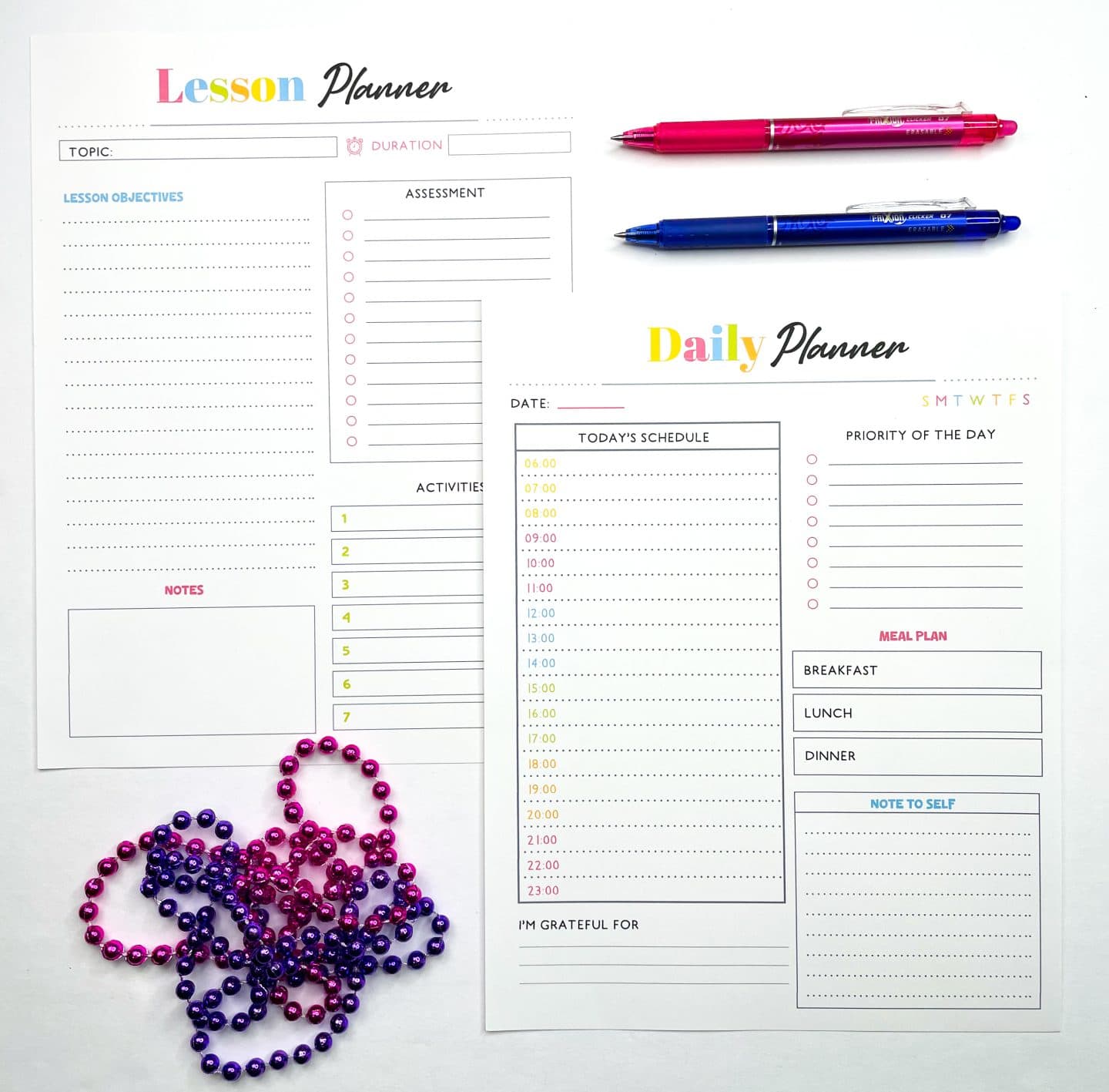 Two printable homeschool planning pages are shown side by side. The left page is a "Lesson Planner" with sections for topic, duration, objectives, assessment, activities, and notes. The right page is a "Daily Planner" with an hourly schedule from 6 AM to 11 PM, priority tasks, meal plan, gratitude section, and a space labeled “note to self.” A pink and a blue pen sit at the top, and strands of pink and purple beads decorate the bottom left.