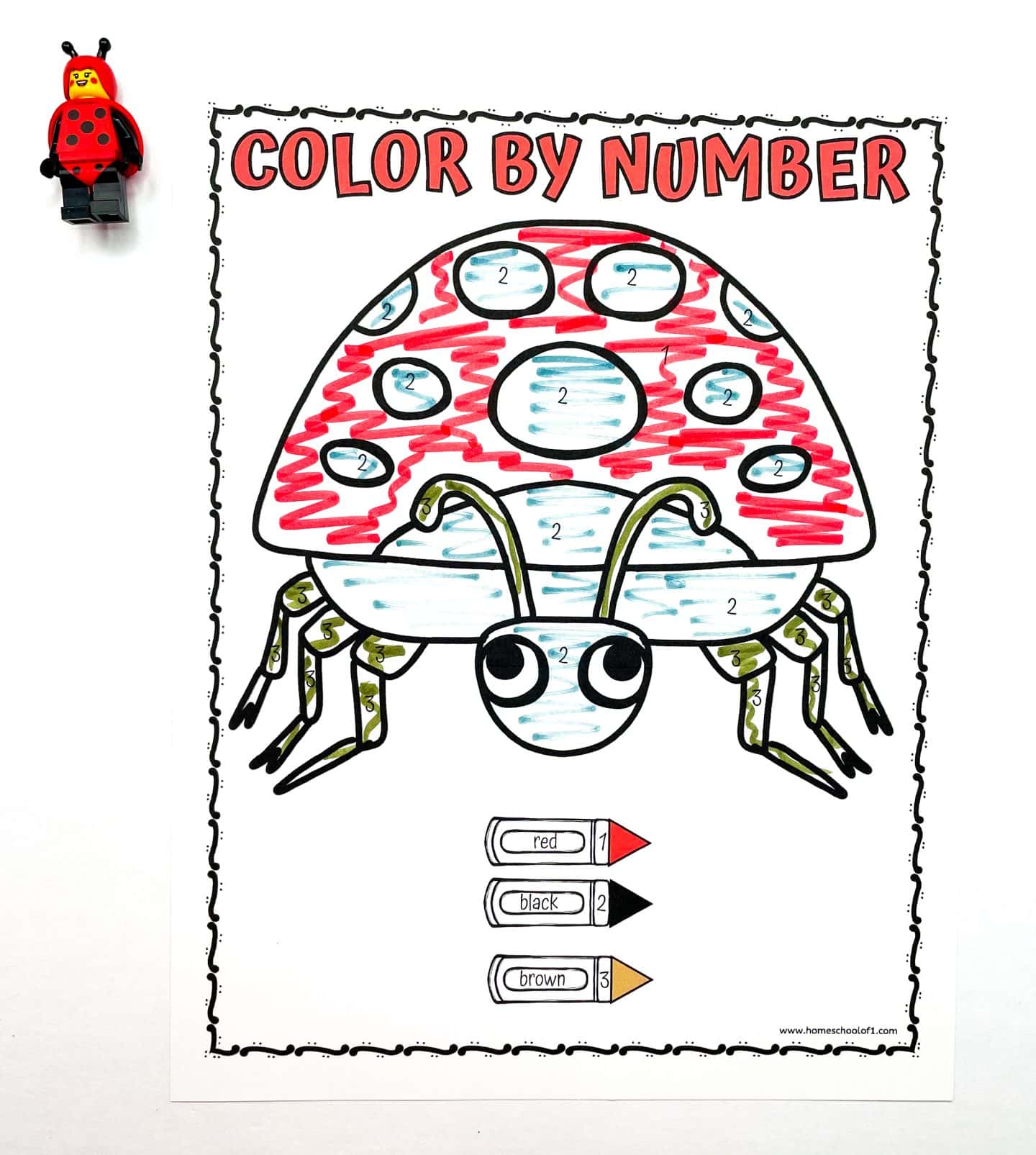 A preschool worksheet titled “Color by Number” features a large cartoon ladybug filled in using a color code: red for number 1, black for number 2, and brown for number 3. The ladybug’s body is mostly red and black with brown and black legs. A LEGO ladybug figure is placed at the top left corner, and the worksheet sits on a white background.