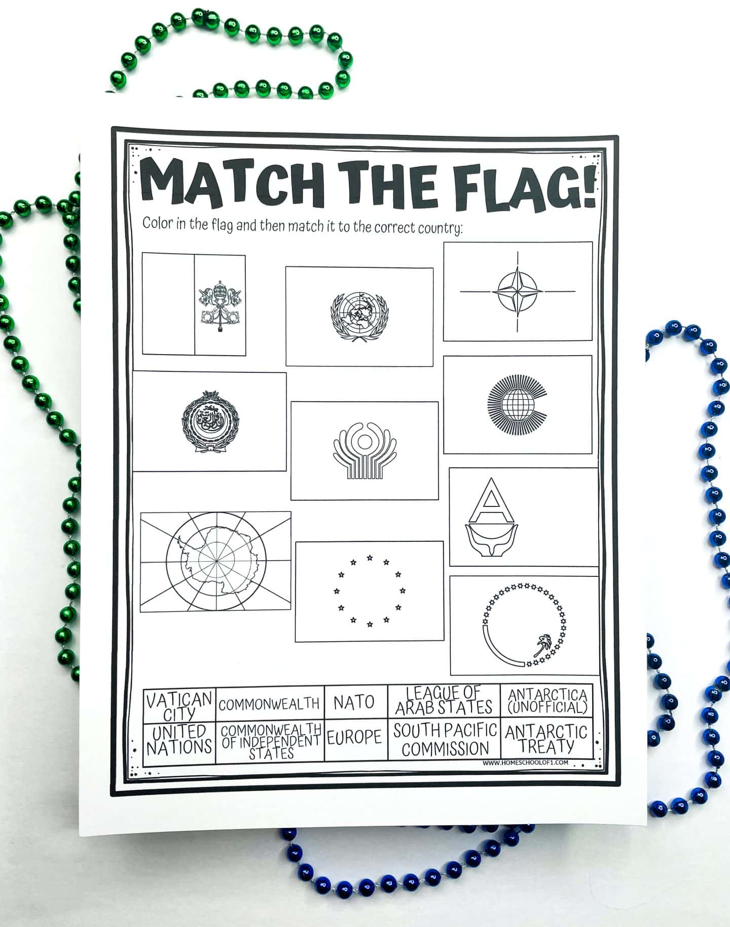 A black-and-white worksheet titled “Match the Flag!” with twelve flag illustrations representing global organizations or entities. Students are instructed to color in each flag and match it to the correct label below. Label options include Vatican City, NATO, United Nations, League of Arab States, Europe, Antarctic Treaty, and others. The worksheet is surrounded by green and blue beaded necklaces.