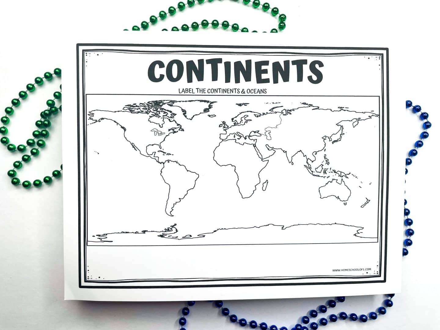 A black-and-white printable worksheet titled "Continents" with instructions to label the continents and oceans. The sheet features an unlabeled world map, showing outlines of all seven continents and surrounding oceans. Green and blue beaded necklaces are placed around the worksheet for decoration.