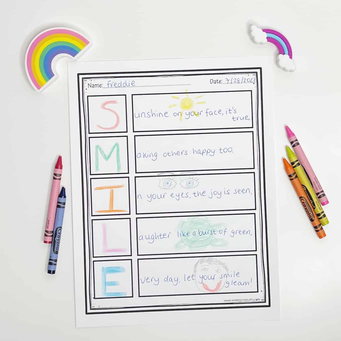 A completed acrostic poem worksheet for kids featuring the word “SMILE,” with colorful letters and hand-drawn illustrations next to each line of the poem. The name “Freddie” and date “7/25/2021” are written at the top. The poem is surrounded by crayons and two rainbow-shaped erasers, creating a bright and cheerful creative setup.