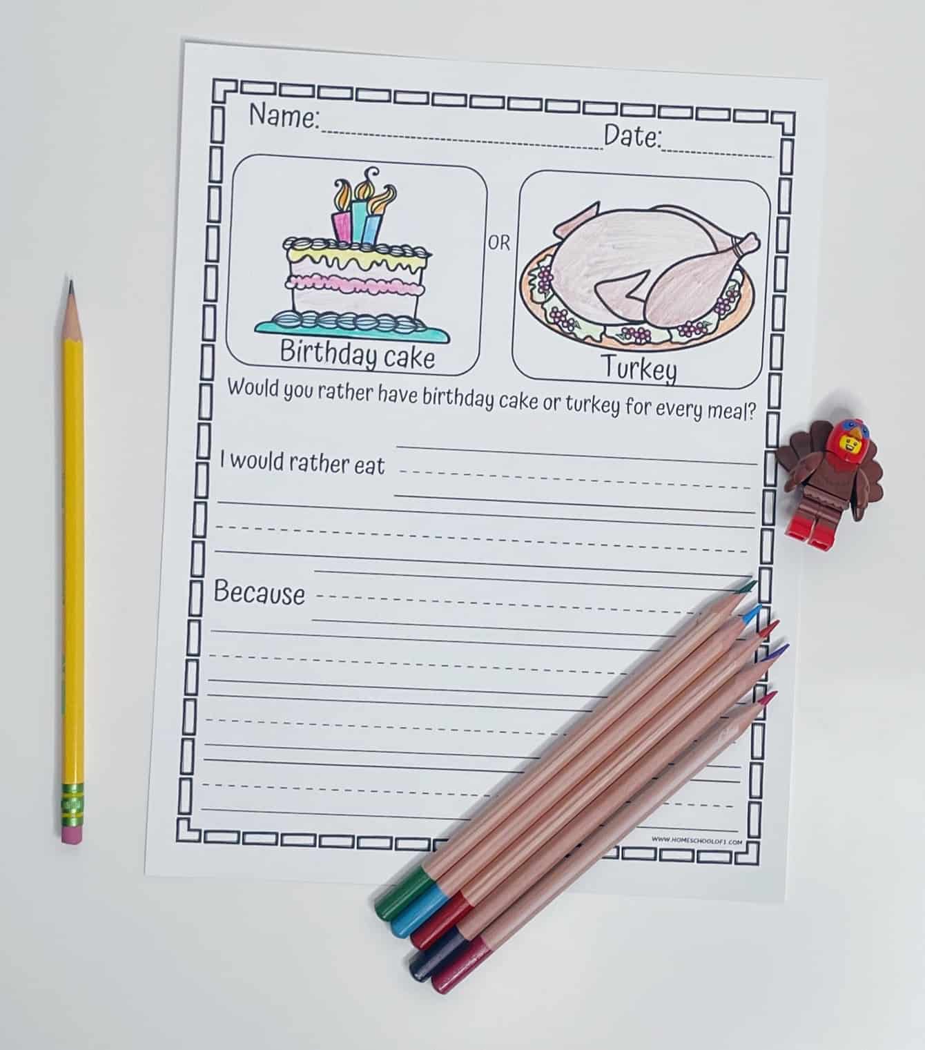 Printable first grade writing prompt worksheet asking “Would you rather have birthday cake or turkey for every meal?” with illustrated images of both options. The sheet includes lines for students to write their choice and reason, with a pencil, colored pencils, and a LEGO-style turkey figure arranged beside it.

