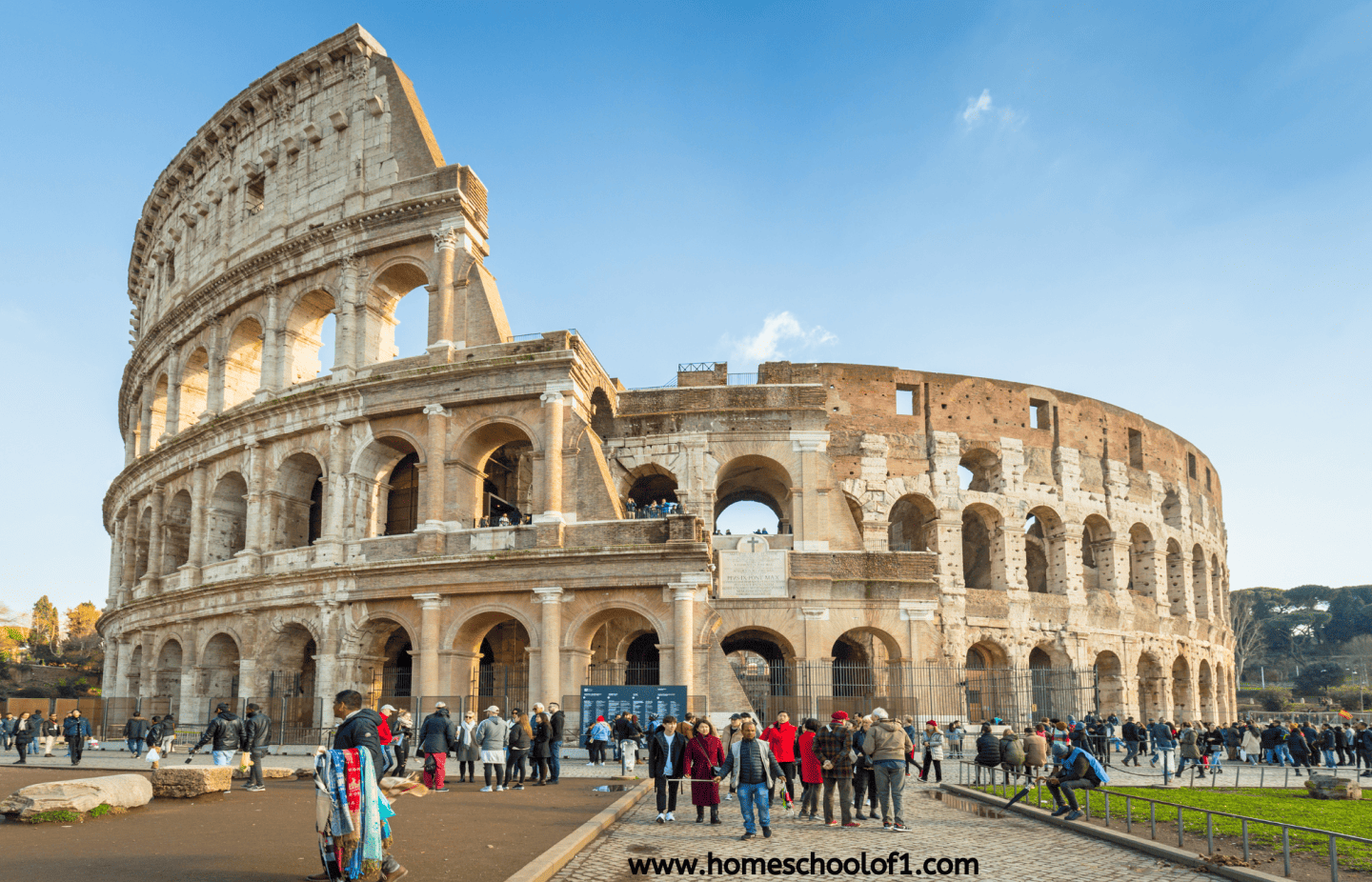 Tourists gather around the Roman Colosseum on a clear day, with the ancient amphitheater prominently lit by the sun.