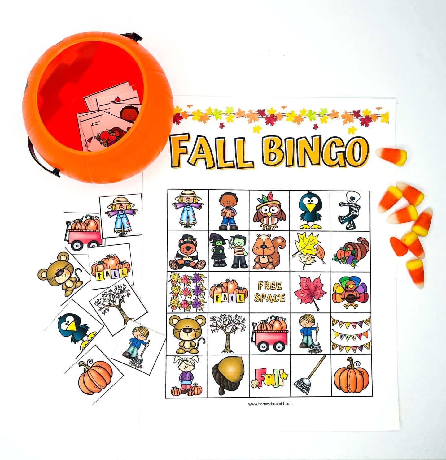 A colorful "Fall Bingo" game is displayed with a bingo card featuring autumn-themed illustrations like pumpkins, scarecrows, owls, turkeys, leaves, and acorns. A small orange plastic pumpkin bucket holds bingo pieces, and several game tiles are spread out beside the card. Candy corn is scattered on the right, adding to the festive fall vibe.