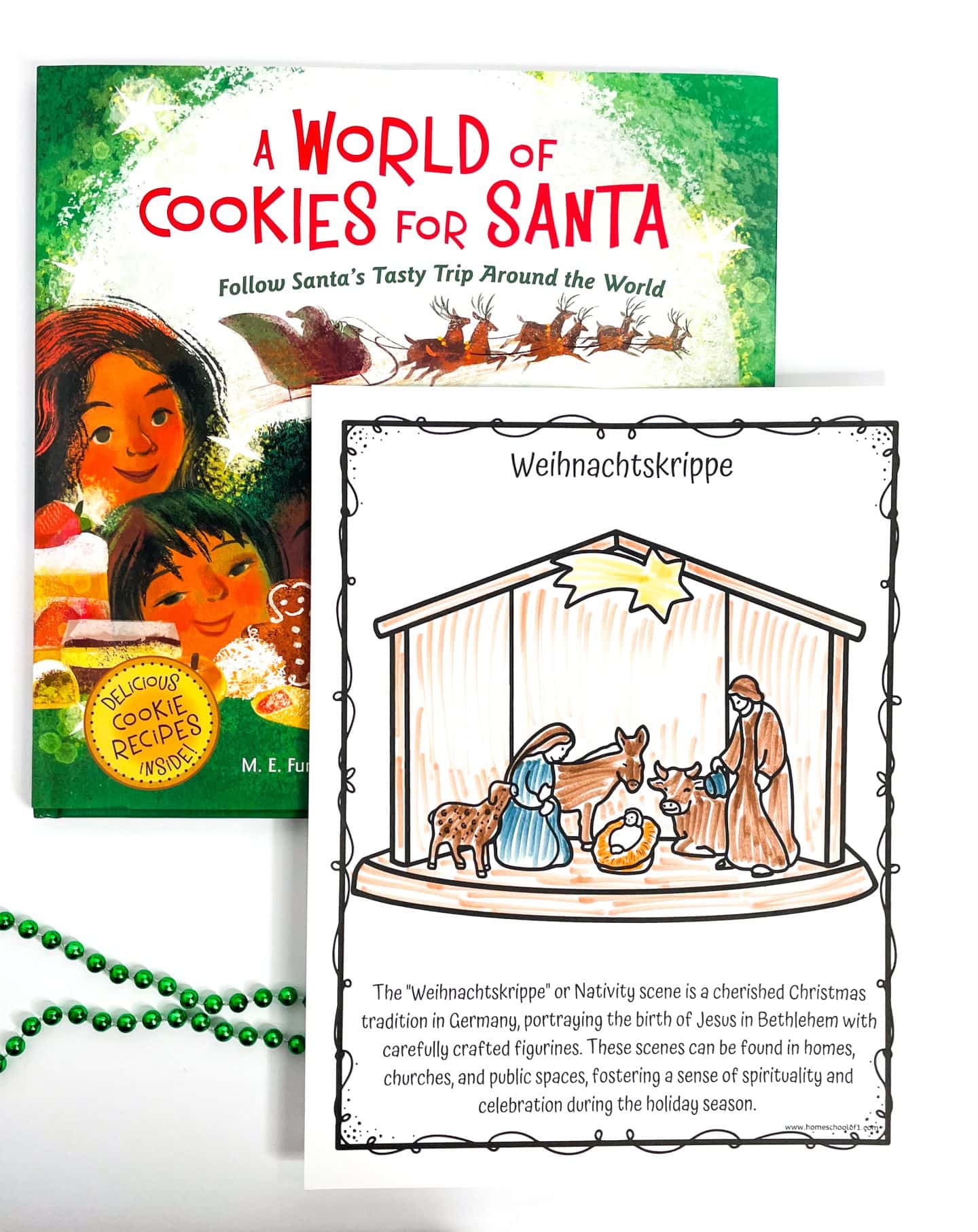 Coloring page of a Weihnachtskrippe, or German nativity scene, featuring Mary, Joseph, baby Jesus, and animals in a stable under a bright star. The text below explains that nativity scenes are a cherished Christmas tradition in Germany, displayed in homes and public spaces. Behind the worksheet is the book A World of Cookies for Santa, and green bead garland lies nearby.