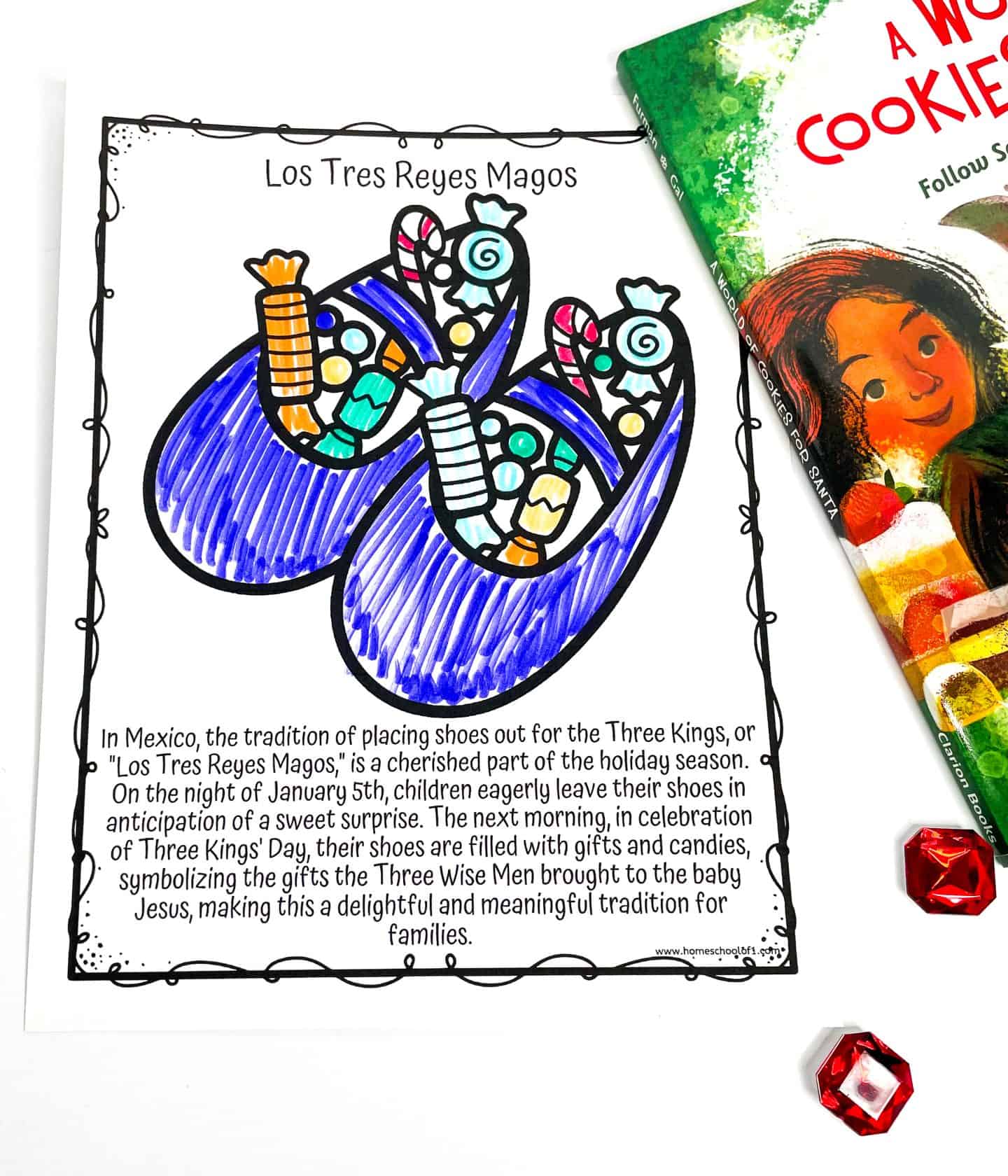 Coloring worksheet titled "Los Tres Reyes Magos" featuring two brightly colored purple shoes filled with candy and gifts. Below the illustration is a description of the Mexican tradition where children leave their shoes out on January 5th to receive surprises from the Three Kings in celebration of Three Kings' Day. A colorful book titled "A World of Cookies for Santa" is partially visible beside the worksheet.

