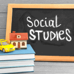 Small chalkboard with the words โSocial Studiesโ written in white chalk, sitting beside a stack of books topped with a miniature yellow car and a model house, symbolizing learning about communities, geography, and economics in a homeschool setting.