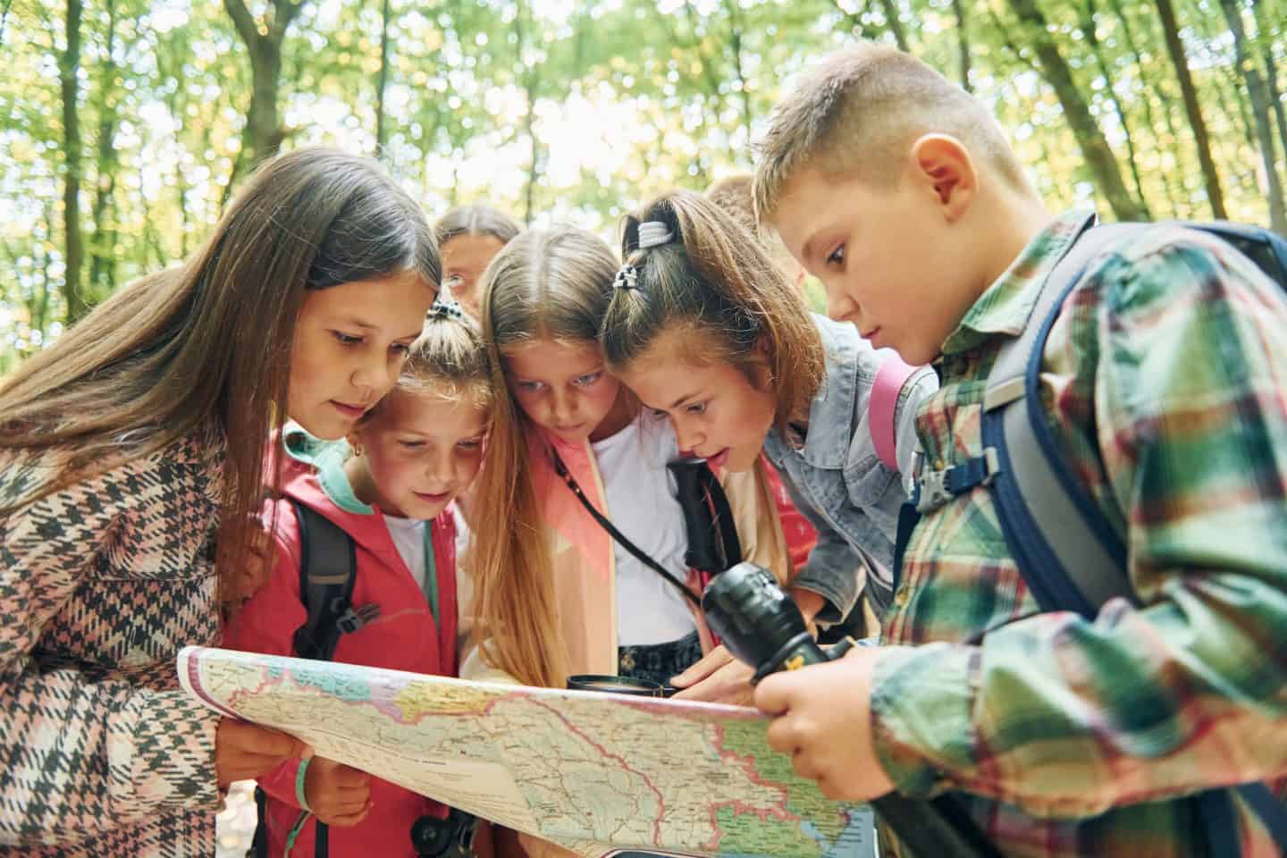 Using map. Kids in green forest at summer daytime together
