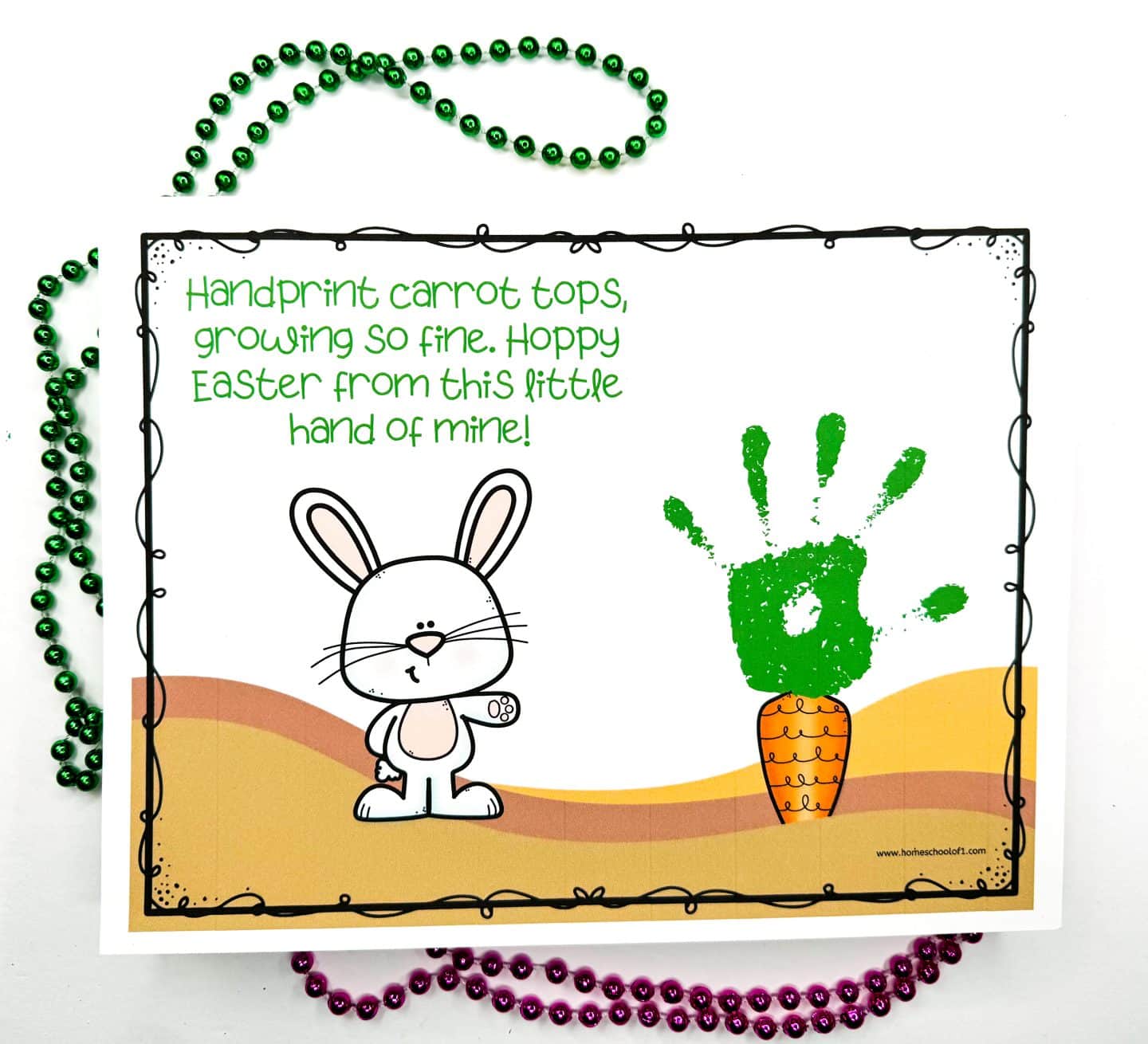 Easter handprint art project featuring a bunny and an orange carrot with a green handprint stamped above it to represent carrot tops. The poem at the top reads, “Handprint carrot tops, growing so fine. Hoppy Easter from this little hand of mine!” Green and pink bead necklaces decorate the background.