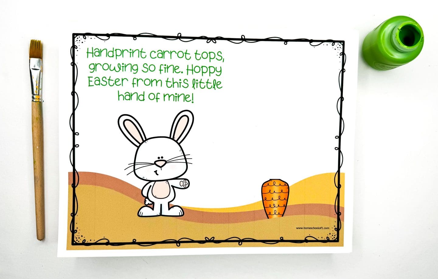 Printable Easter handprint art template featuring a cute bunny next to a carrot in a hilly background. The top text reads, “Handprint carrot tops, growing so fine. Hoppy Easter from this little hand of mine!” A green paint bottle and paintbrush are placed beside the page, ready for kids to stamp their painted handprint above the carrot.