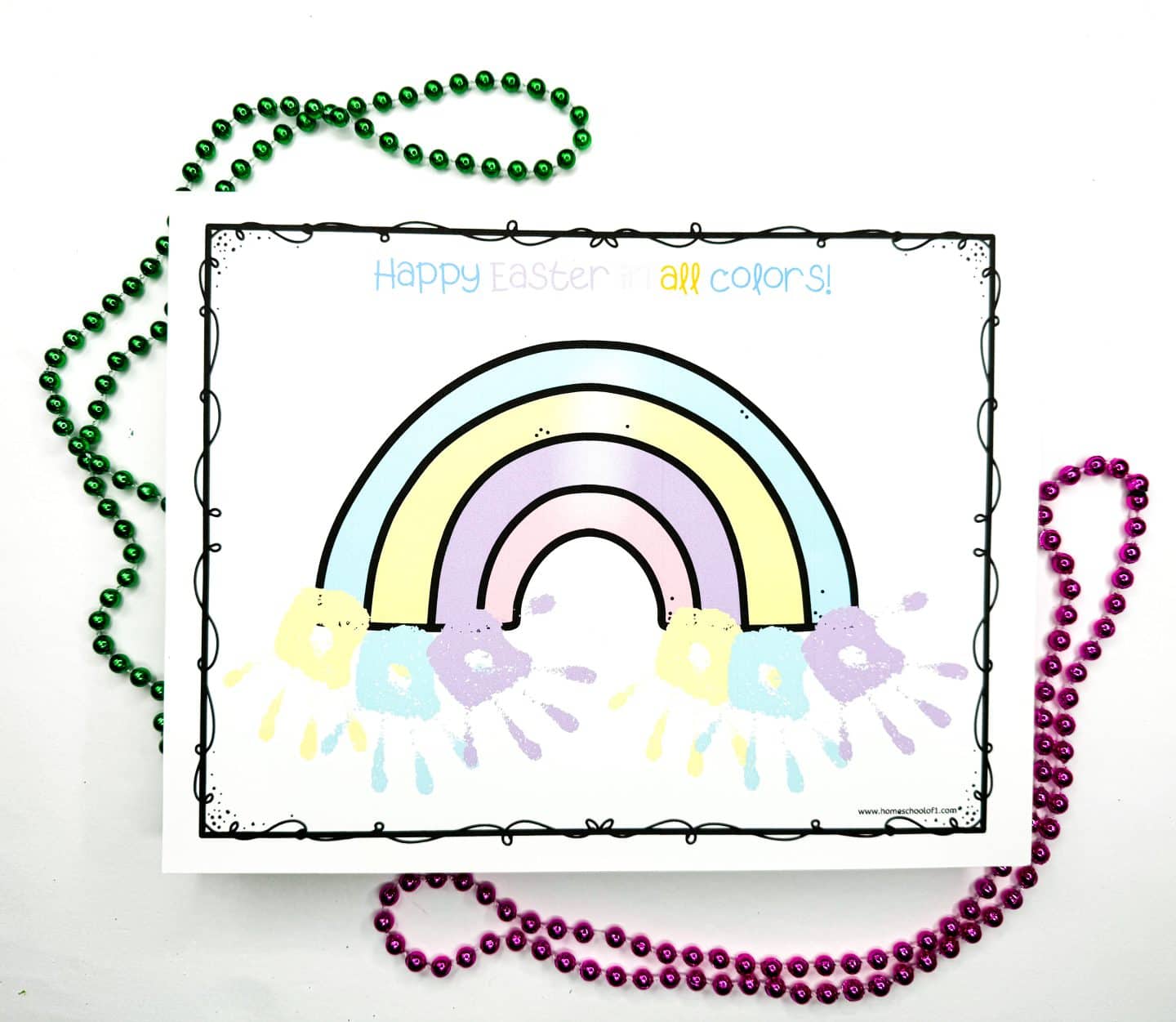 Completed Easter handprint art showing a pastel rainbow with yellow, blue, purple, and white handprints stamped beneath each arch, creating a colorful and festive base. The phrase “Happy Easter in all colors!” is written in soft multicolored letters above. The artwork is surrounded by green and pink beaded necklaces.