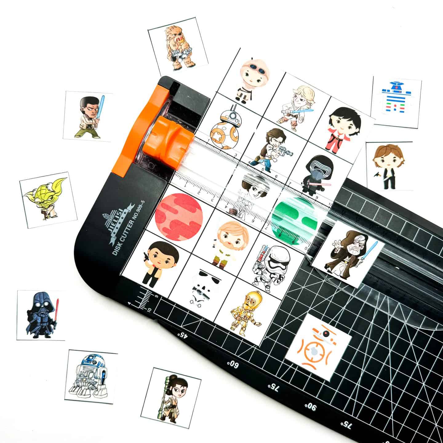 A bingo card is being trimmed on a cutting board tool, with several Star Wars character squares already cut out. Characters include Kylo Ren, Yoda, Rey, and BB-8, all in a cute, cartoon style.

