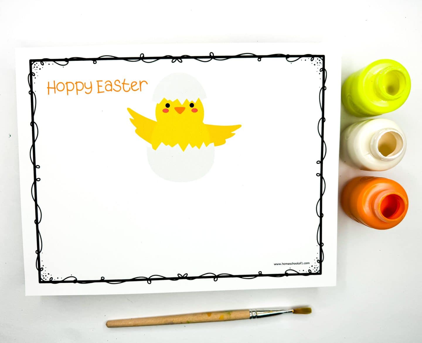 Easter handprint art template featuring a cute yellow chick hatching from a white egg, with the phrase “Hoppy Easter” written in orange at the top. The setup includes three paint pots in yellow, white, and orange, along with a paintbrush, suggesting it's ready for kids to add painted handprint wings to complete the chick design. 