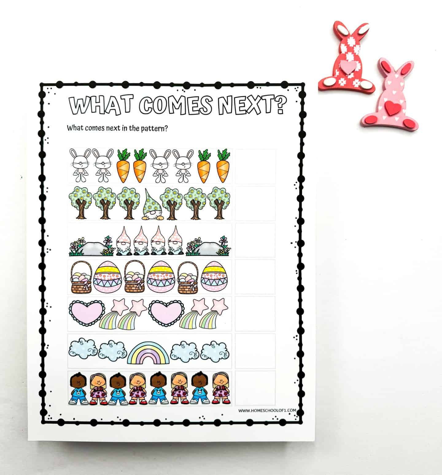 A colorful Easter pattern recognition worksheet titled "What Comes Next?" featuring rows of repeating images such as bunnies and carrots, trees and mushrooms, gnomes and rocks, Easter baskets and eggs, hearts and rainbows, clouds and rainbows, and diverse children in Easter attire. Two decorative bunny clips in pink sit in the upper right corner.