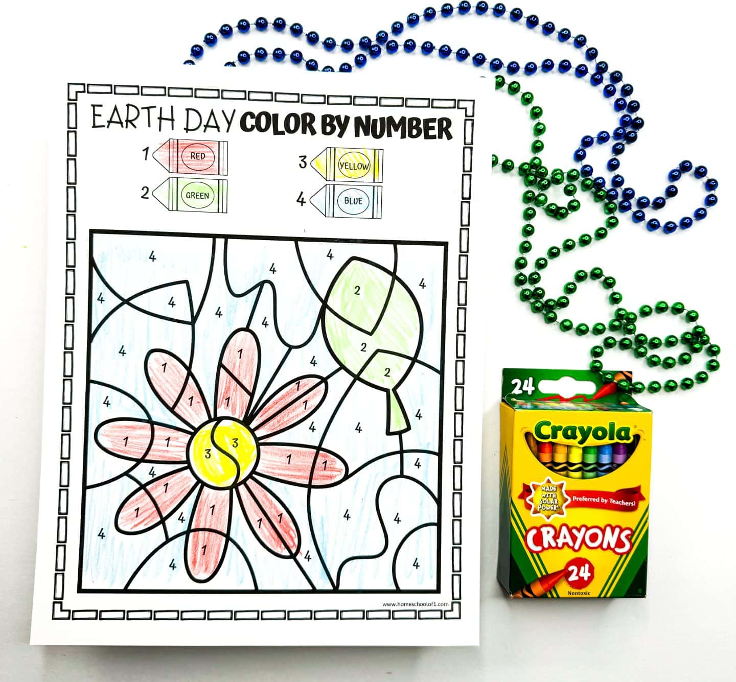 Earth Day color by number worksheet featuring a large flower with red petals, a yellow center, and green leaves and stem. The background is shaded light blue. A crayon key at the top assigns red, green, yellow, and blue to numbers 1 through 4. The sheet is accompanied by green and blue bead strands and a box of 24 Crayola crayons.