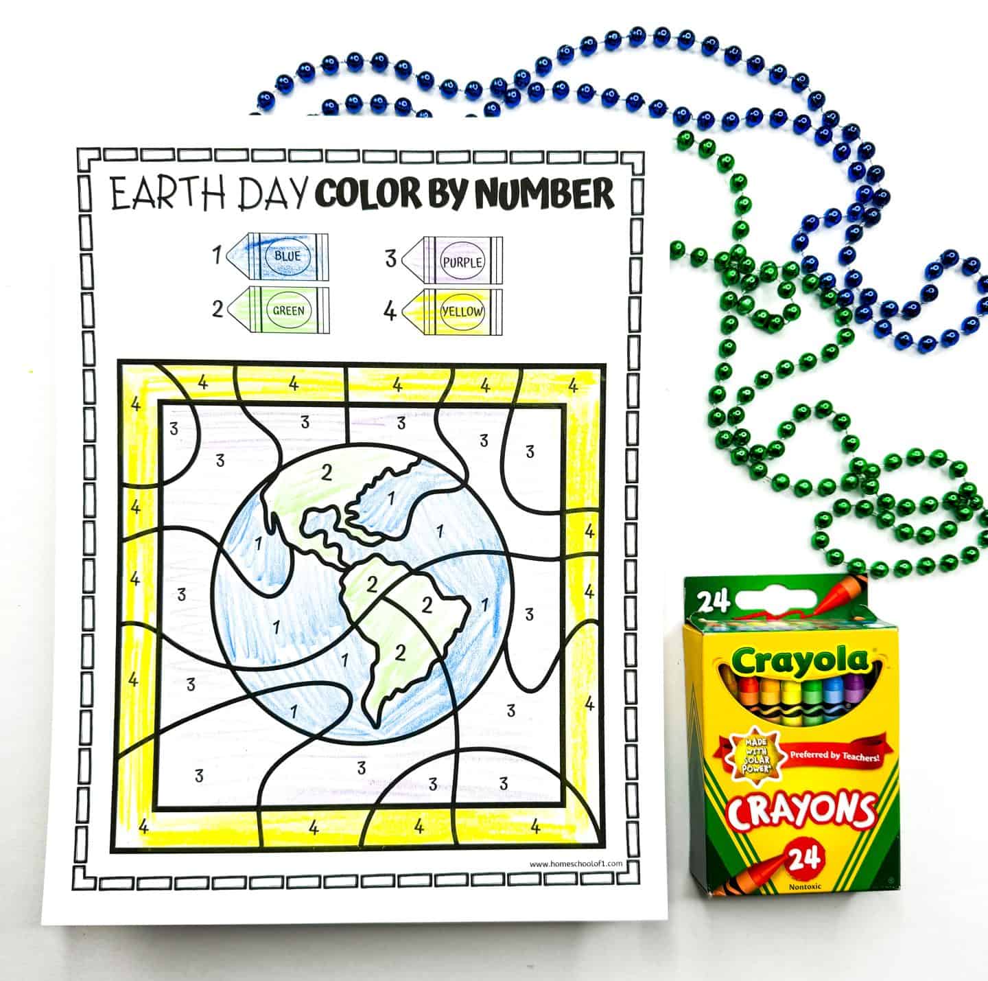 Completed Earth Day coloring by number worksheet featuring a globe with continents colored green and oceans in light blue. The background is yellow, and numbered sections match the provided color key using Crayola crayons. Perfect for Earth Day classroom activities, coloring practice, and educational number recognition for kids. Green and blue beaded necklaces and a box of 24 Crayola crayons are placed beside the page.