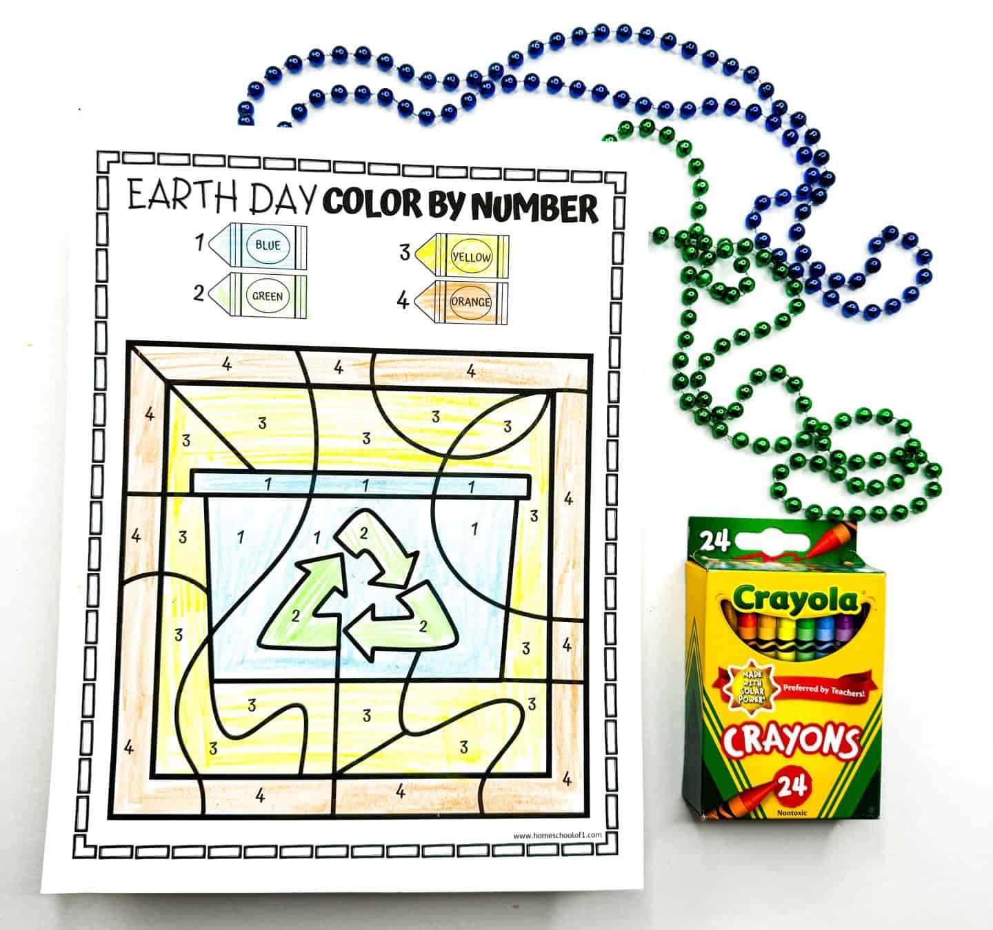 Earth Day color by number printable featuring a recycling bin with a green recycle symbol in the center. The background is colored using a palette of blue, green, yellow, and orange, corresponding to numbers 1 through 4 shown in a crayon key at the top. The page is surrounded by green and blue bead strands and a 24-pack of Crayola crayons.