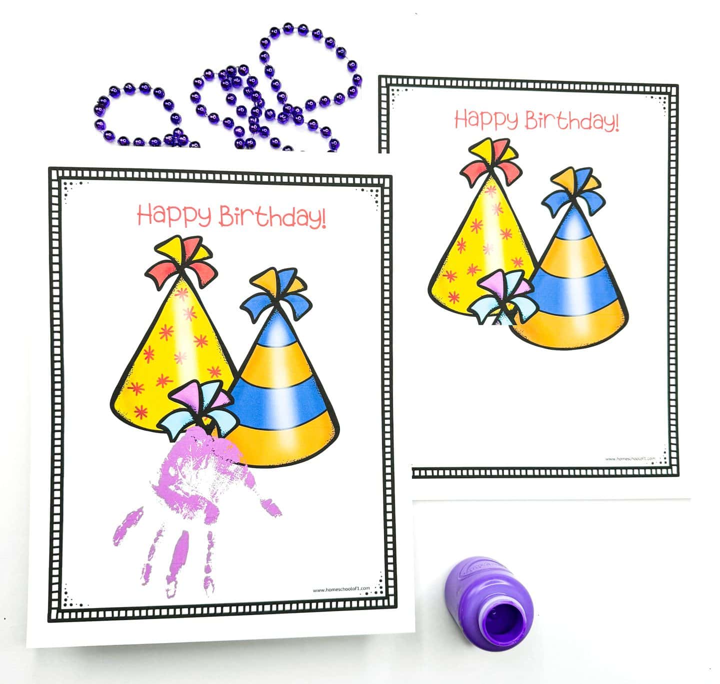 Colorful birthday handprint printables featuring two party hats with bows and the phrase “Happy Birthday!” One sheet includes a purple handprint underneath the hats as a personal touch, while the other is blank for kids to add their own. Purple beads and a matching paint bottle complete the festive craft setup.