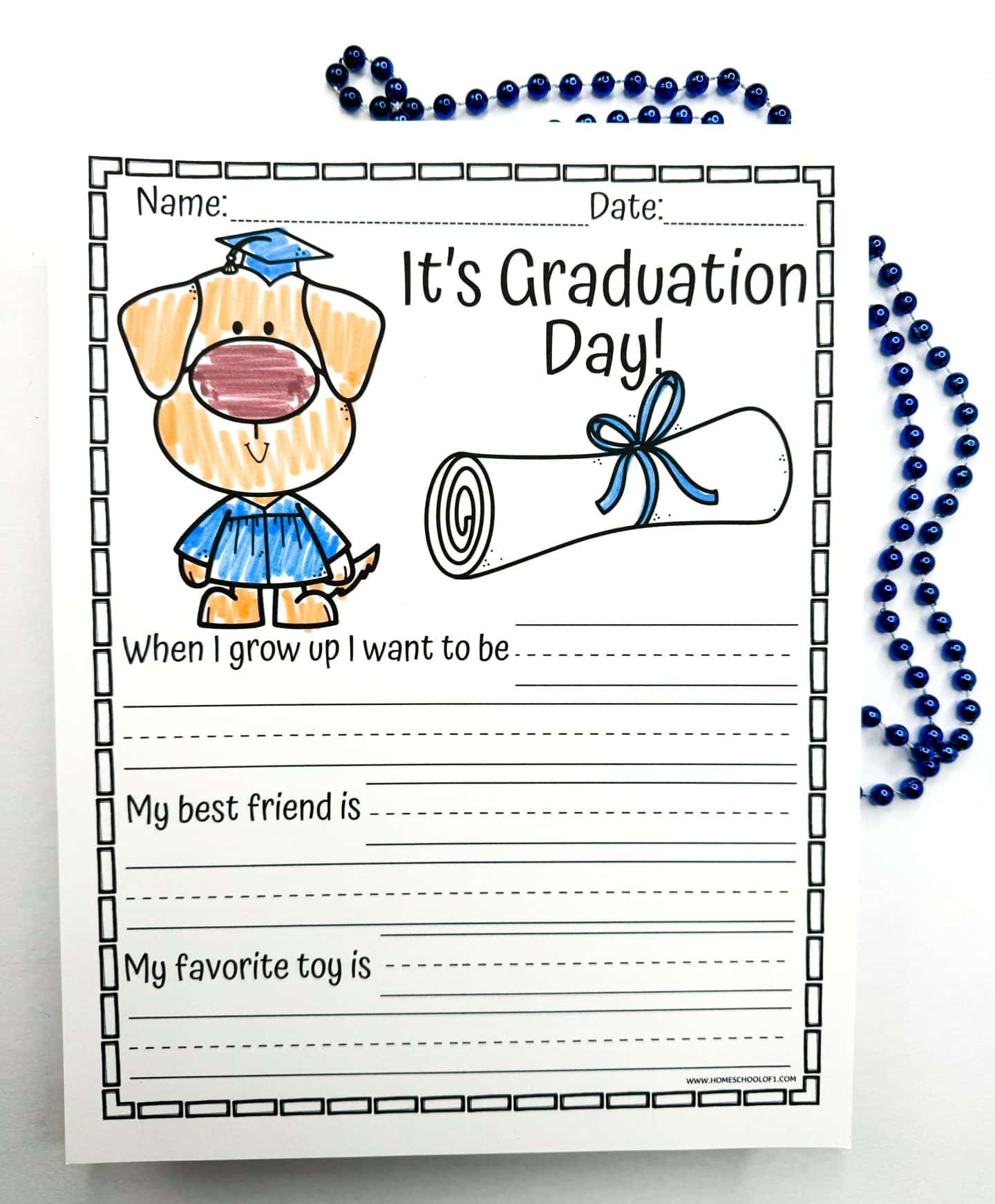 A kindergarten graduation writing prompt worksheet featuring a cartoon dog in a blue graduation cap and gown, next to a rolled-up diploma tied with a blue ribbon. The worksheet prompts children to answer "When I grow up I want to be," "My best friend is," and "My favorite toy is," with lines provided for writing, and is decorated with strands of blue beads.