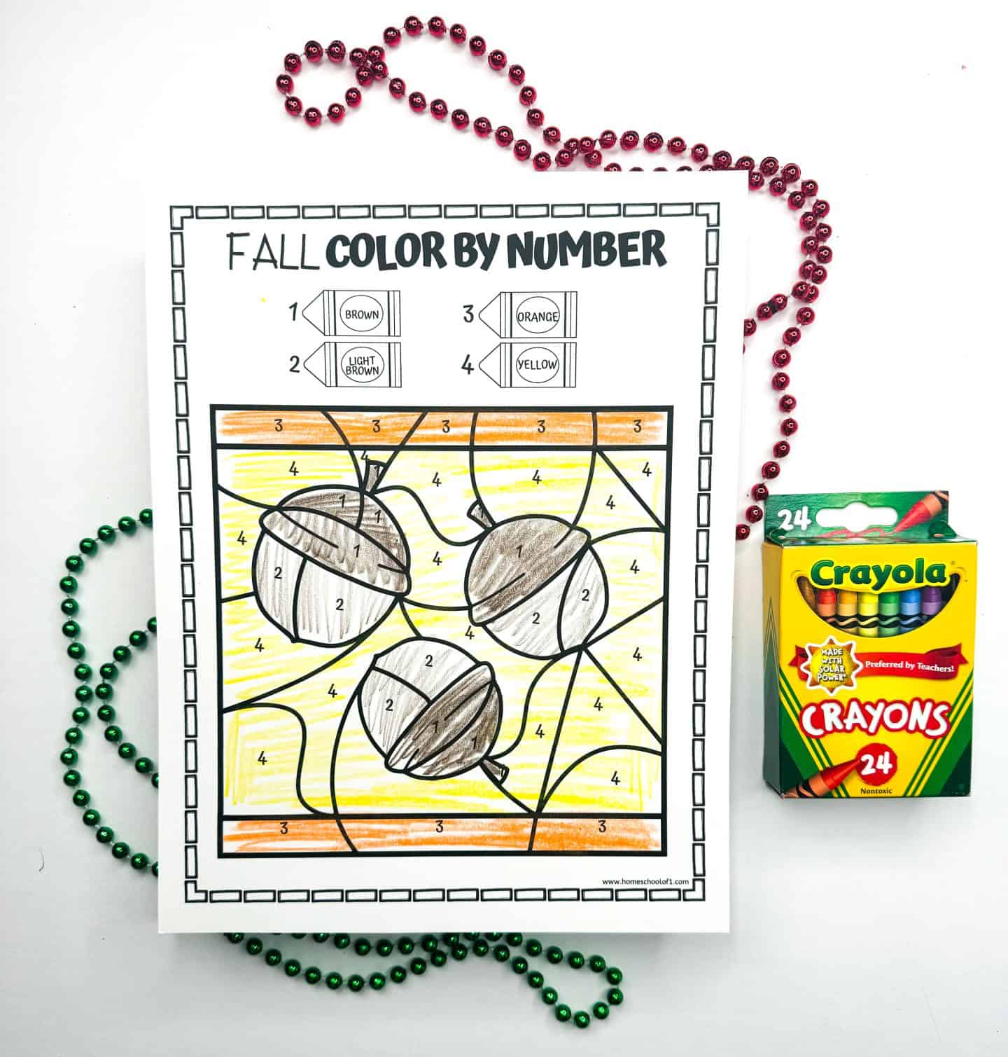 A fall-themed color by number printable with acorns ready to be colored, flanked by festive bead necklaces and a Crayola crayon pack.