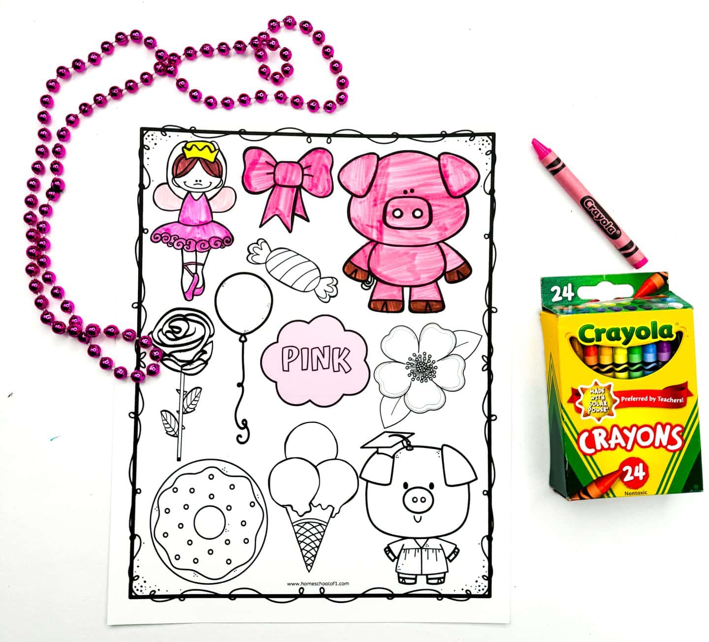 A pink worksheet features outlined images including a ballerina, bow, pig, rose, and a cloud labeled pink, with several items partially colored using a pink crayon. A strand of shiny pink beads is looped beside the sheet, and a 24-count Crayola crayon box is placed to the right. The activity is designed for young children to learn and recognize the color pink through fun illustrations.