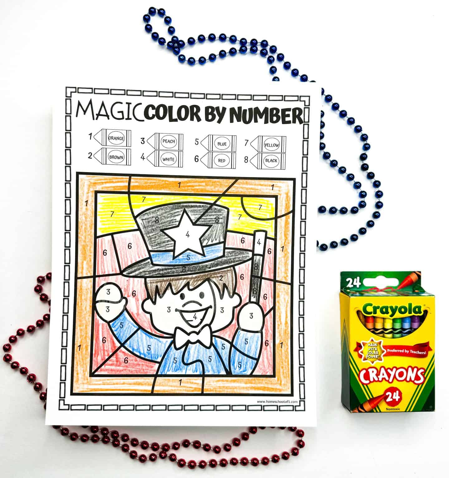 Colored worksheet of a smiling magician in a top hat with a star, displayed alongside decorative beads and a box of 24 Crayola crayons.