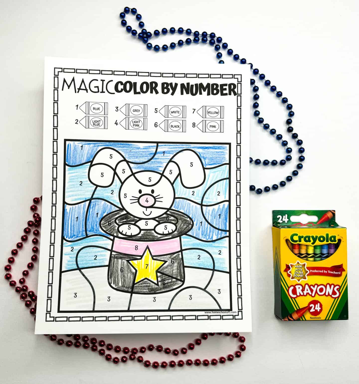 A completed color by number sheet with a rabbit in a magician's hat, flanked by bead necklaces and a Crayola crayons box.