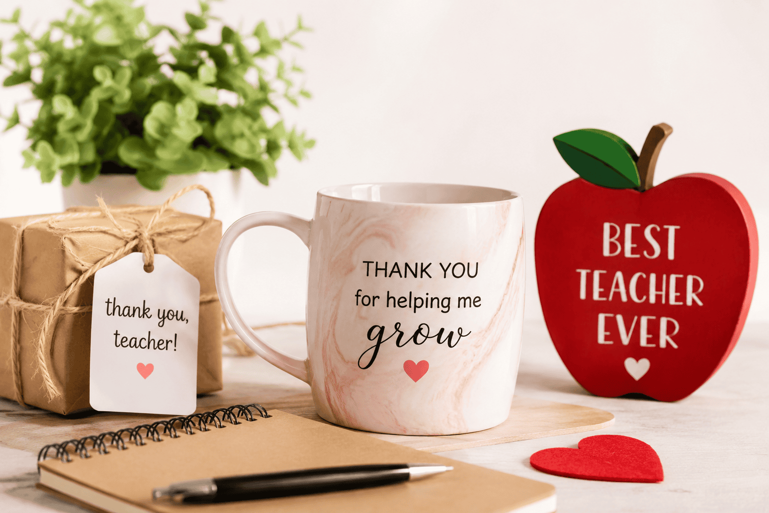 Thoughtful teacher appreciation gifts including a thank you mug, wrapped gift, notebook, and teacher apple sign on a bright tabletop.